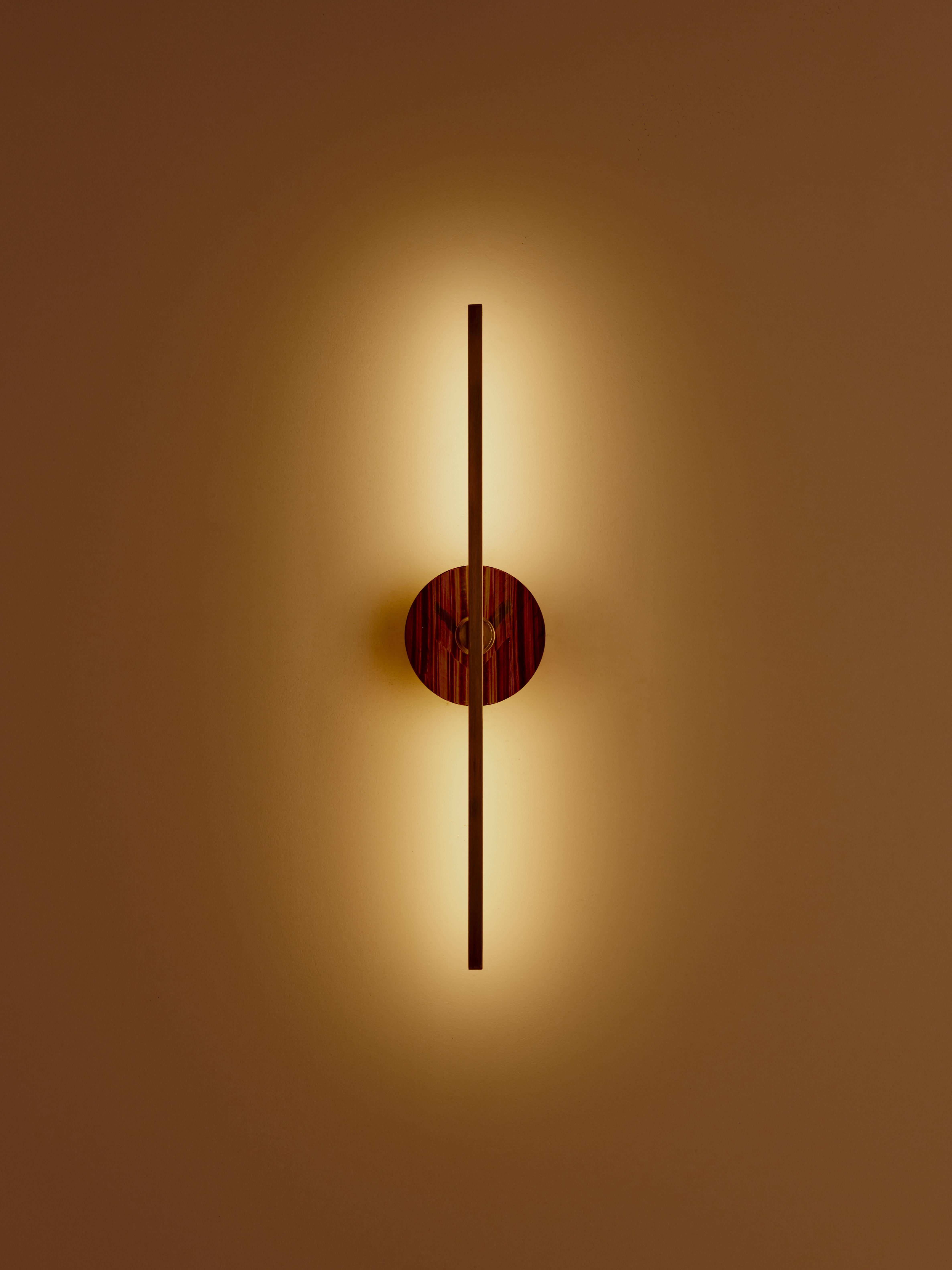 The Elite Stick wall sconce combines the minimalism of thin brass profiles with the functionality and power of led technology, offering a warm and diffused light. The tiger eye, pure decorative element, embellishes the structure of the product with