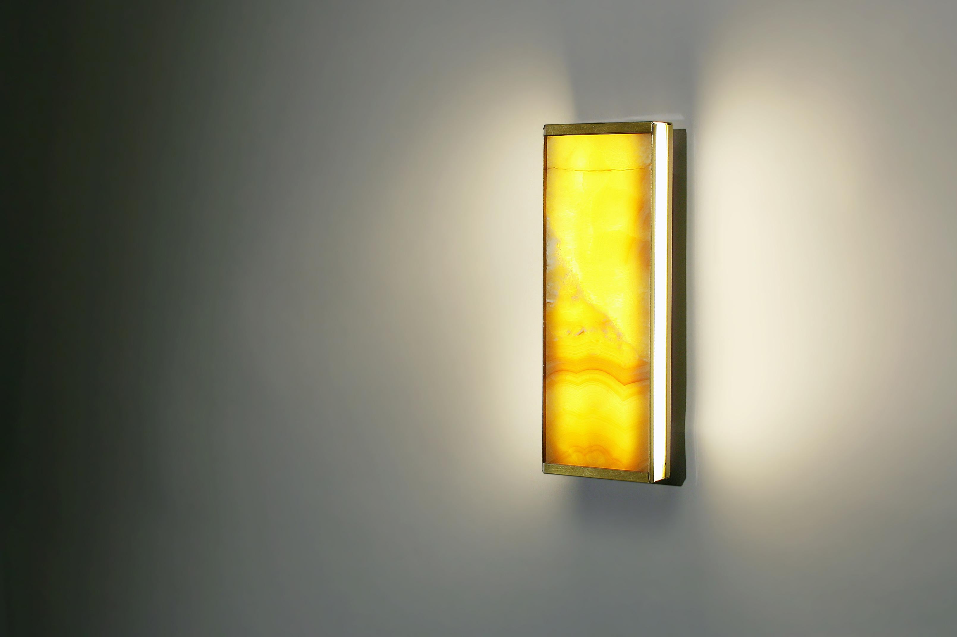 The Tech short wall sconce is a lighting fixture that was designed to merge the luminaire and lampshade into a singular unit, using the translucent properties of ultra-thin veined yellow onyx to create an interplay of light and shadow that
