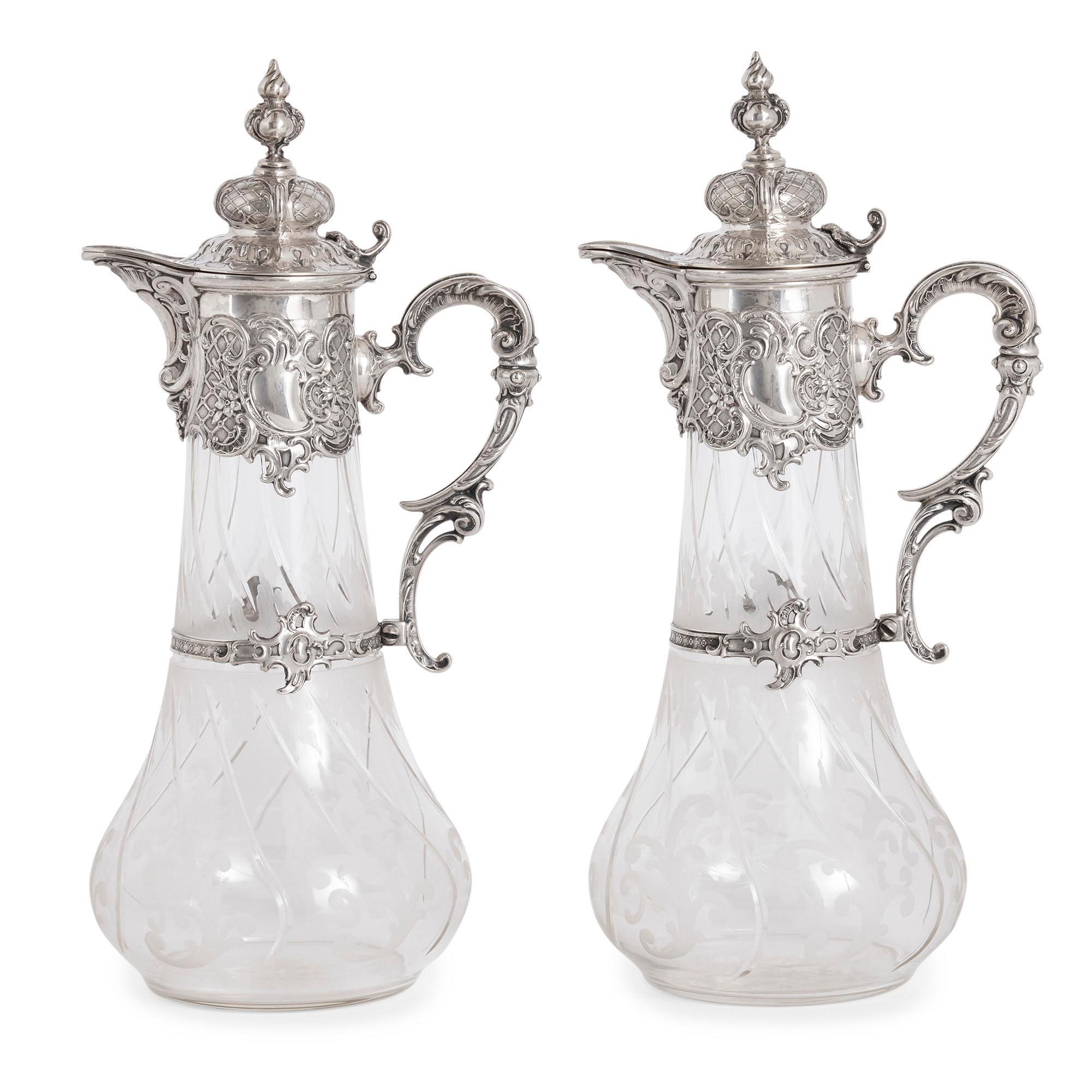 Pair of etched glass and silver pitchers by Bruckmann & Söhne
German, circa 1900
Measures: Height 33cm, width 17cm, depth 14cm

The pitchers, or claret jugs, in this pair by Bruckmann & Söhne are of traditional form, each crafted from silver