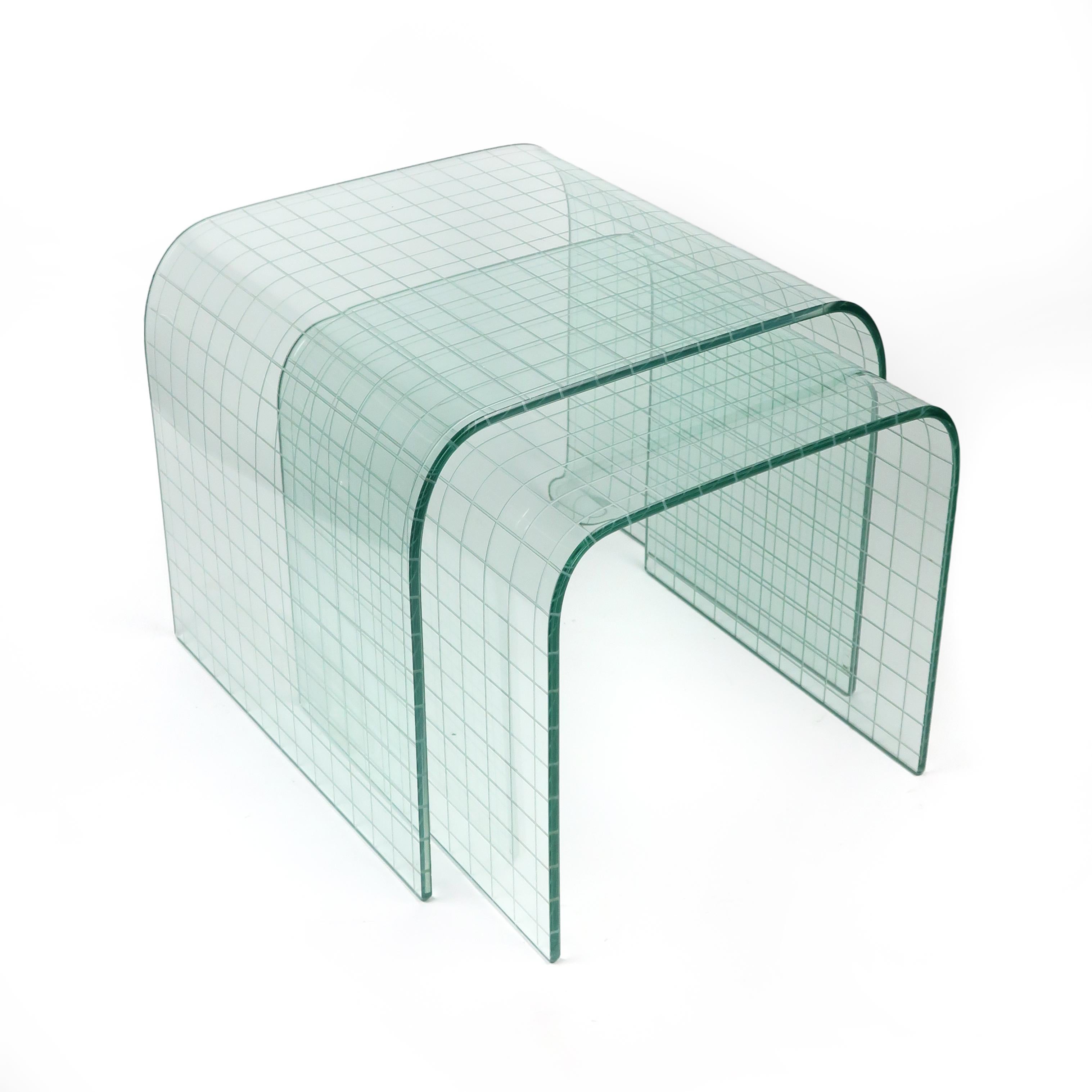 A beautiful 1970s pair of glass waterfall side or nesting tables designed by Italian designer and architect Angelo Cortesi for FIAM of Italy. Each table has an etched grid pattern on its underside and larger one retains original 