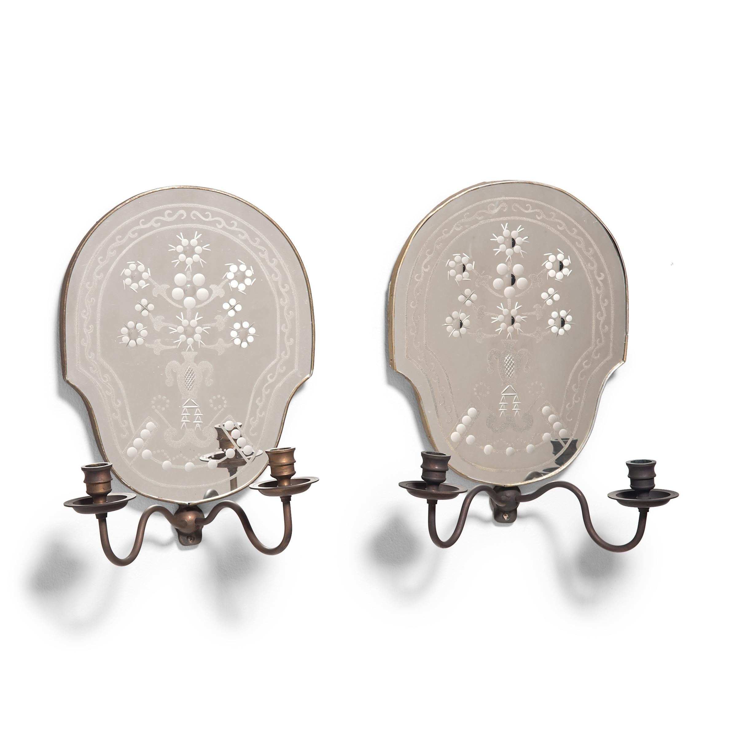 Delicate and refined, these contemporary wall-mounted candle sconces by Vaughan are designed with decorative mirrored backings in the tradition of Venetian etched mirrors. The mirrored backings have a rounded, oblong shape and are etched, cut, and