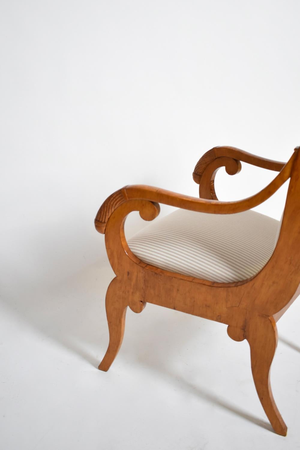 Pair of armchairs in natural wood and veneer with slightly rounded backs decorated with marquetry of facing griffins surrounding a laurel wreath in a frame of foliage and flowers. Armrests and armrest consoles with facing crooks. Belt inlaid with a