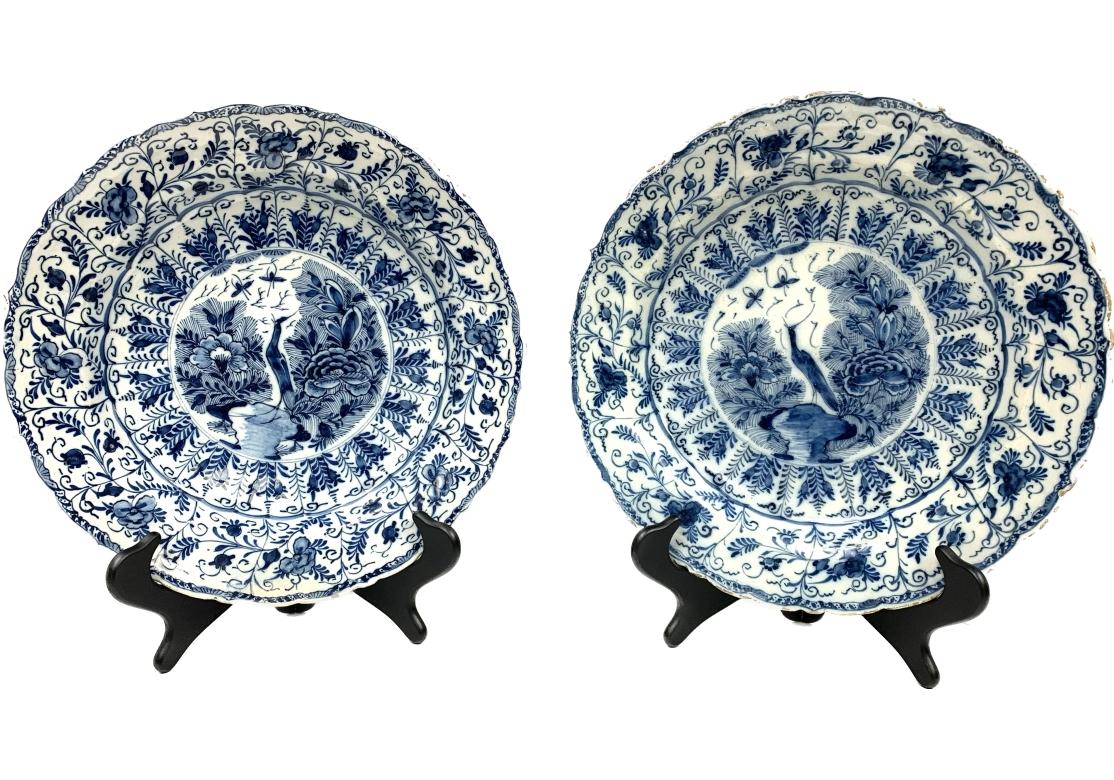 Pair of blue and white chargers with central exotic bird, dragonflies, flowering shrubs surrounded by ferns, leaves and scrolls. The border decorated with repetitive and alternating flowers, vines and leaves.
The plate with scalloped edge and deep