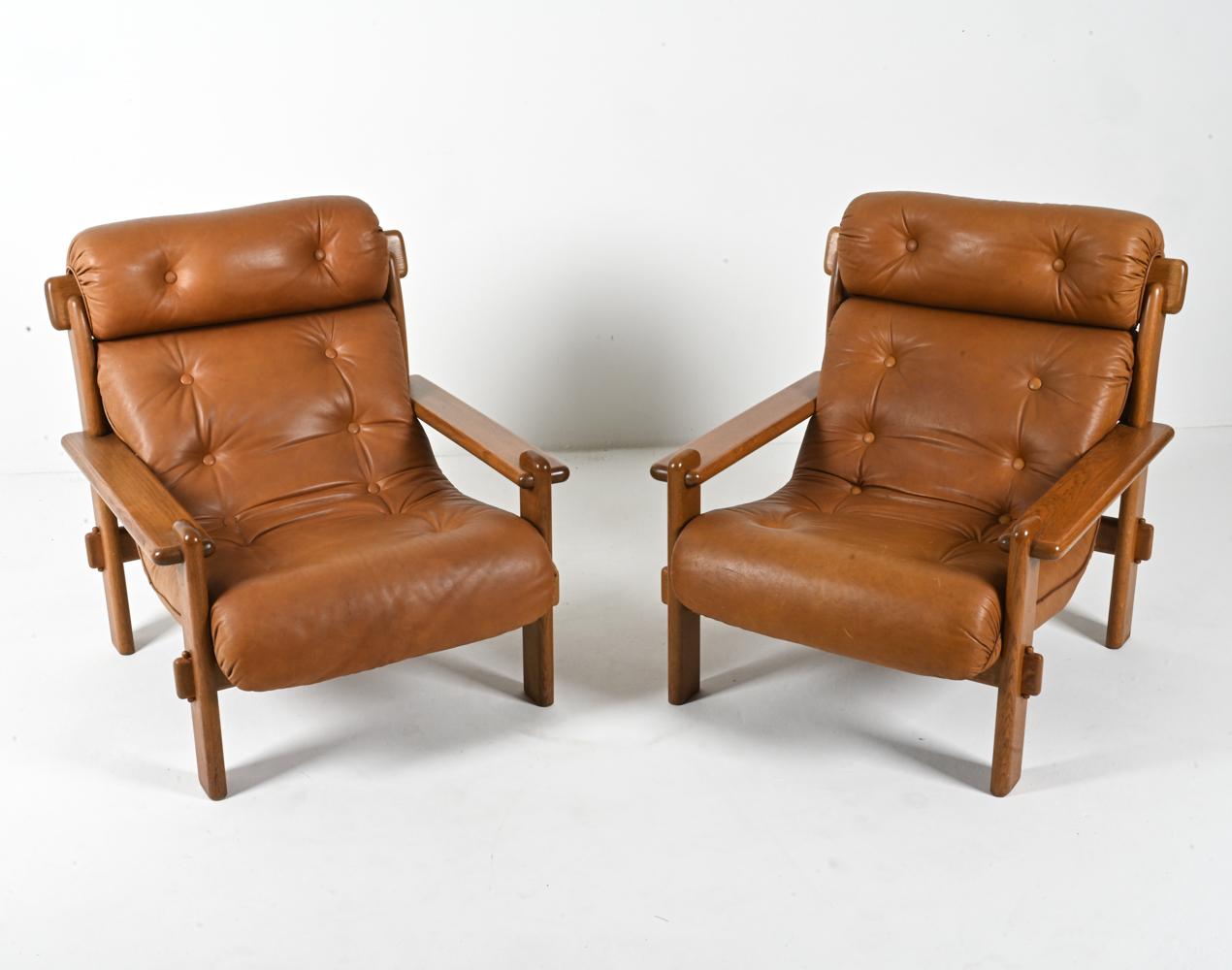 Introducing a stunning pair of Brutalist lounge chairs that effortlessly blend form and function. Crafted in Europe in the 1970s, these chairs boast a substantial frame made from solid oak. The open arms and exaggerated mortise joints add an
