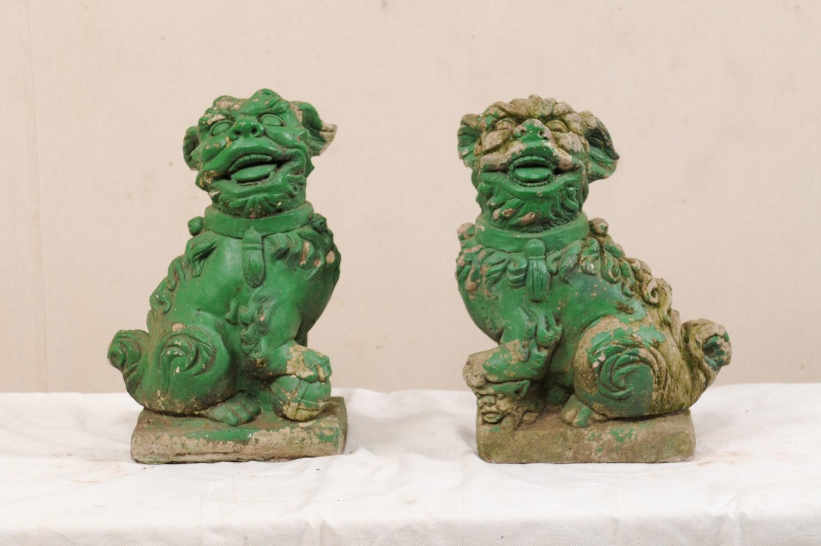 A European pair of Foo Dogs from the mid-20th century. This vintage pair of guardian lions from Europe, created of cast-stone, feature each dog in side-sitting position with expressive faces reflected in their open mouths with teeth and tongue