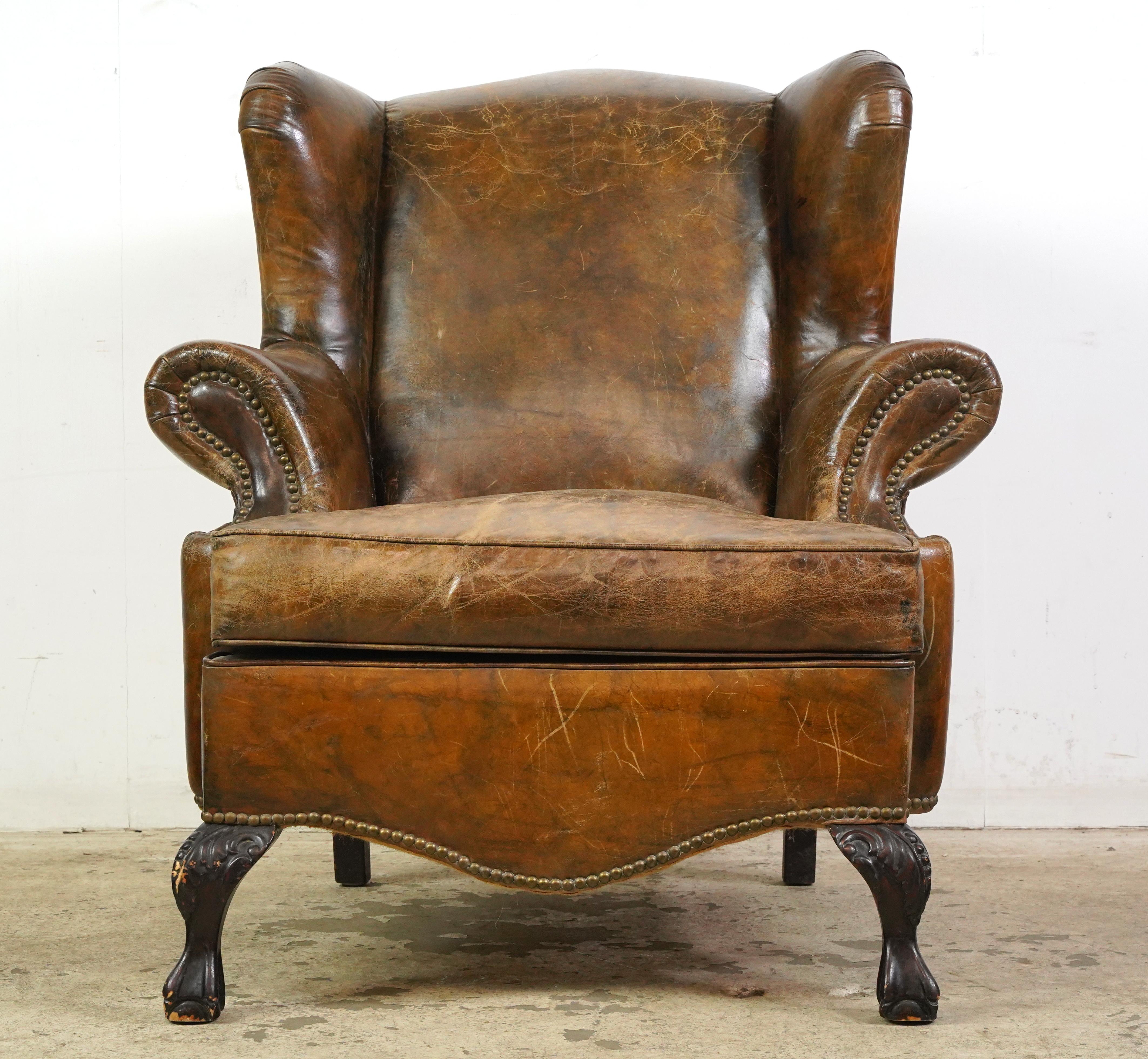 Georgian style brown leather studded club chairs made in France. They feature sloped arms with studded fronts and wooden cabriolet legs. The leather and feet show some signs of wear and age. Please refer to the pictures for a full view of the