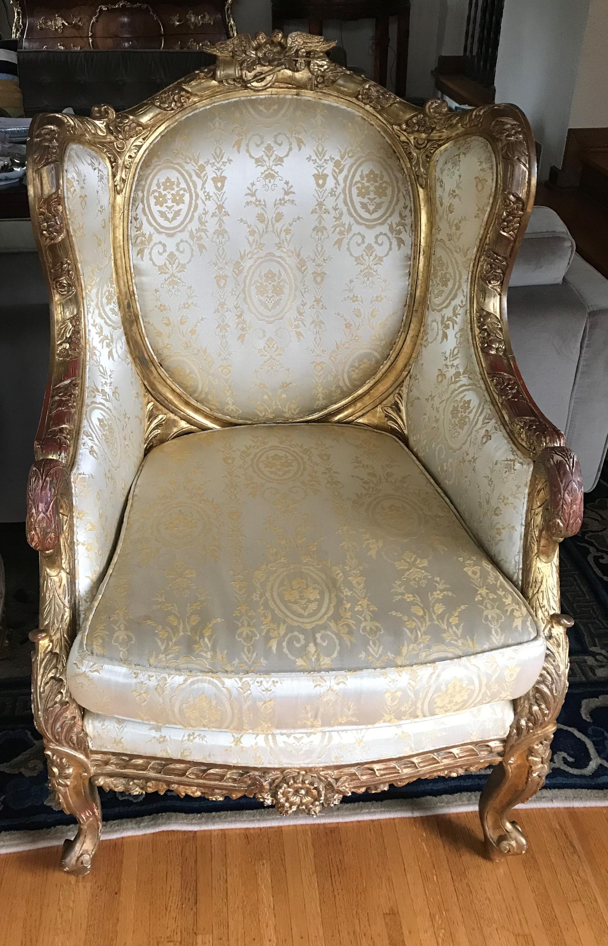 Gorgeous pair of antique European upholstered armchairs. Gold gesso over wood. Swan arms, lovebirds at top. Upholstered in a gold fabric, cushion seat.

19th century in date. Lovely old wear with spots of the red bole showing through. Solid