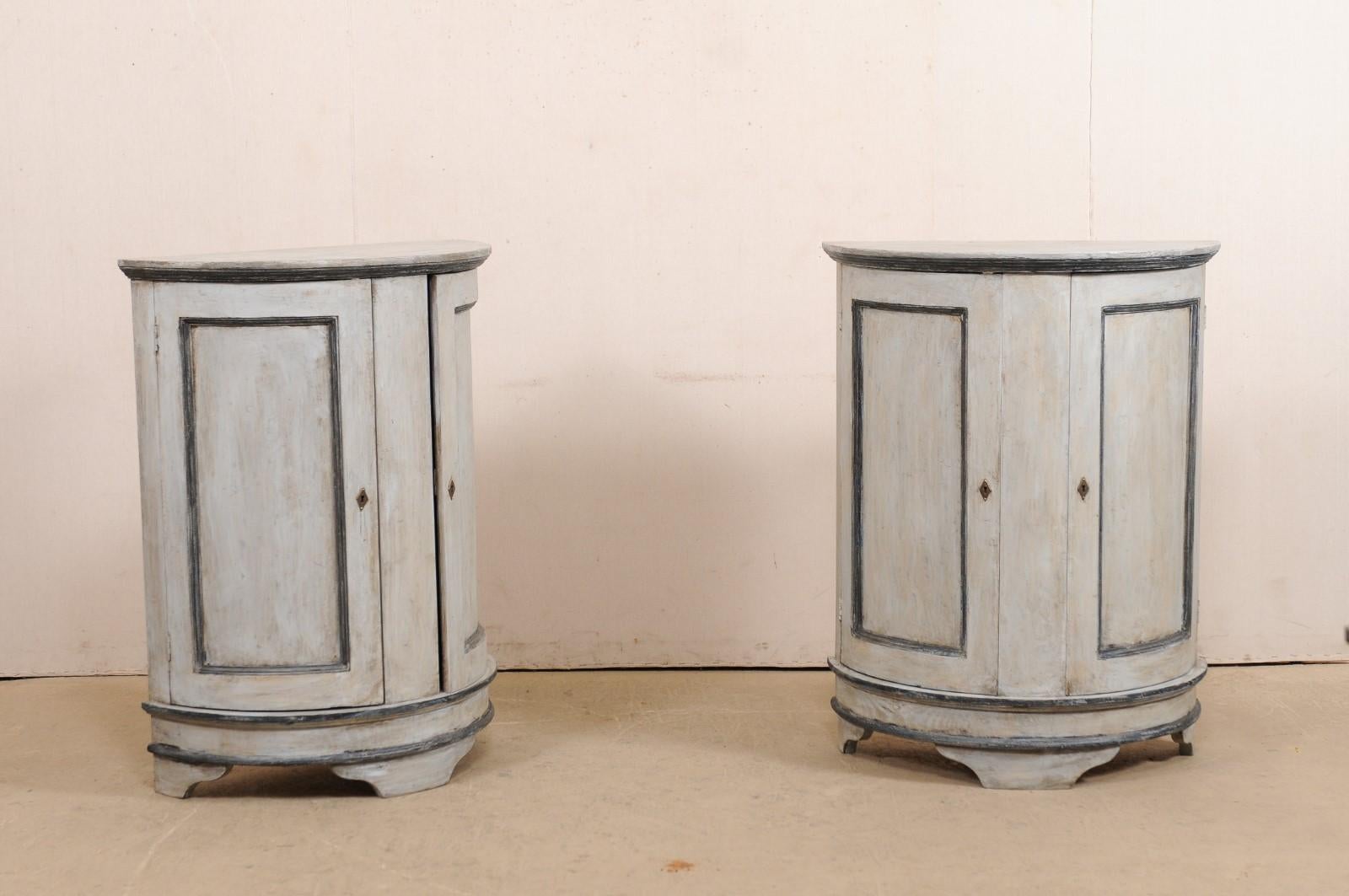 A pair of vintage European painted wood demilune cabinets. This pair of Swedish-style cabinets from Europe each features a half-moon shaped top over a half-mood case which is fitted with a pair of curved and recessed paneled doors, one at each side