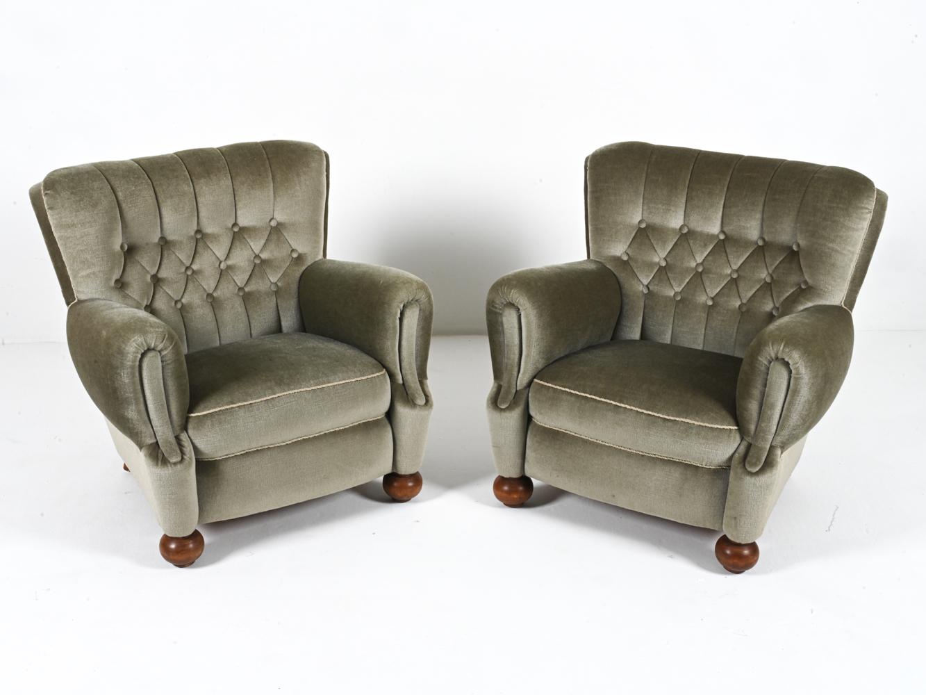 This fabulous pair of Early Modern club chairs features a subtle winged silhouette, with rolled slope arms and bun-style front feet. They are expertly finished in a luxurious sage green mohair, with diamond-tufted backs that give extra texture and