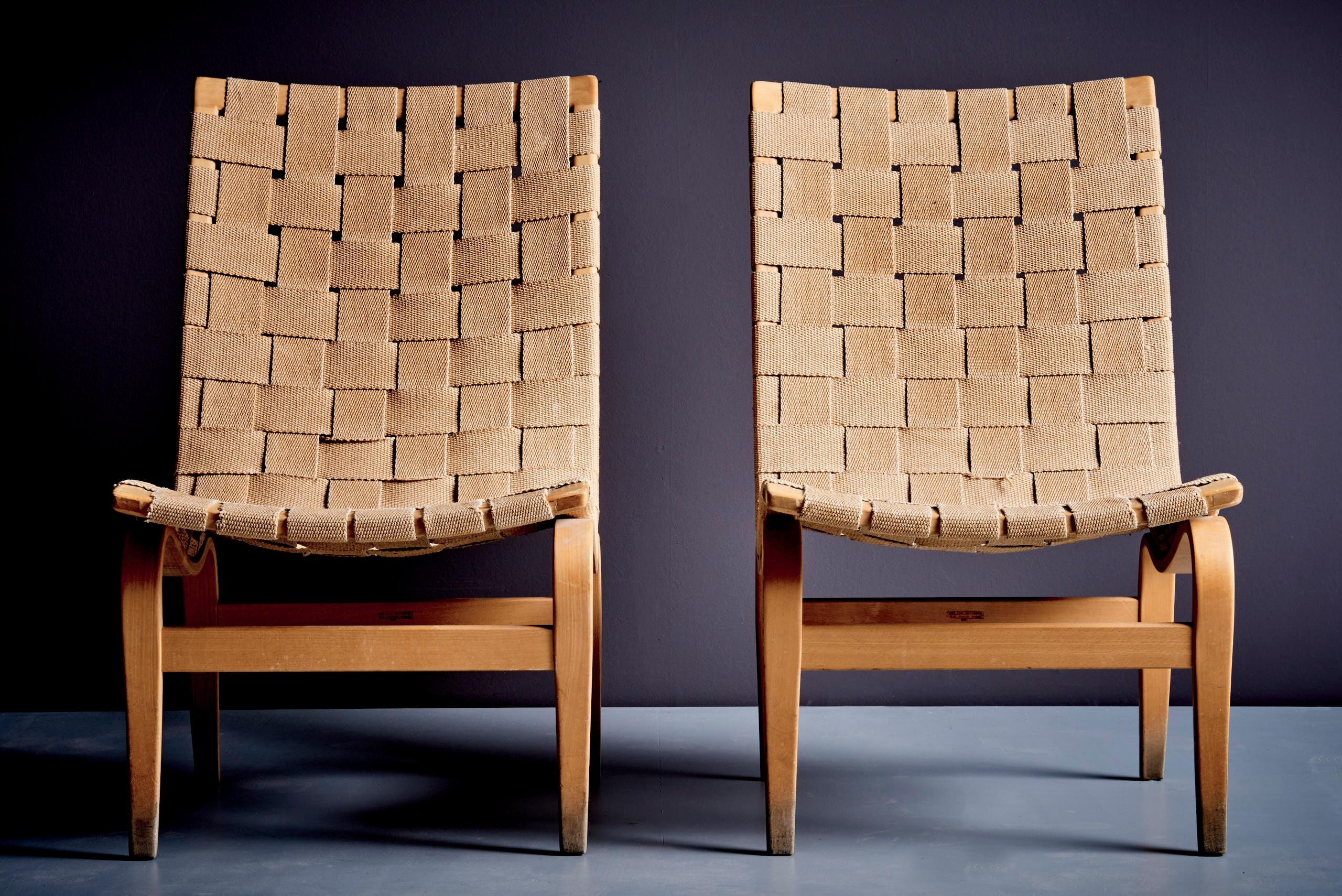 A classic pair of Eva lounge chairs designed by Bruno Mathsson in 1934 made of bent laminated beechwood frames and seats in woven natural hemp webbing, offering both lightness and ergonomic comfort. The webbing shows signs of age and use, consistent
