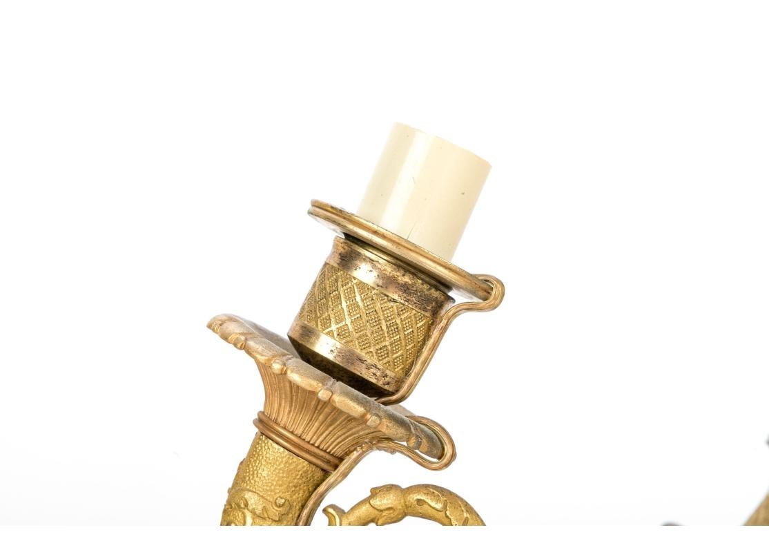 Chaque applique est dotée d'un support en forme de corne nervurée et patinée, avec rosette et collier doré, et est fixée à une plaque arrière circulaire décorée de feuilles d'acanthe et de fleurs doré. L'extrémité patinée se déplace au niveau de la