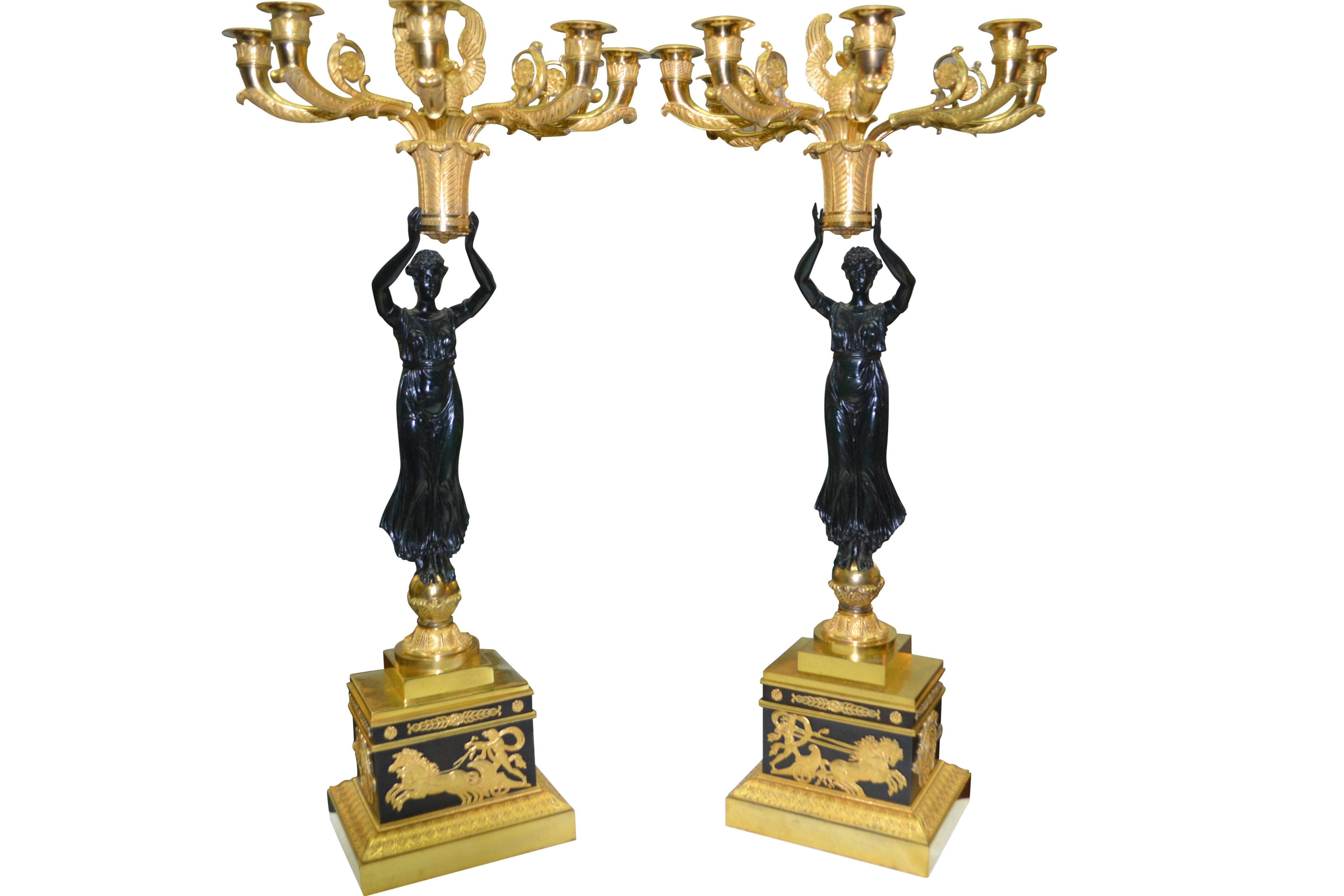 These are a pair of exceptional early French Empire candelabra featuring patinated bronze classically draped maidens holding aloft a gilt bronze plumed basket supporting six candle arms capped by a most unusual open winged swan finial. The whole
