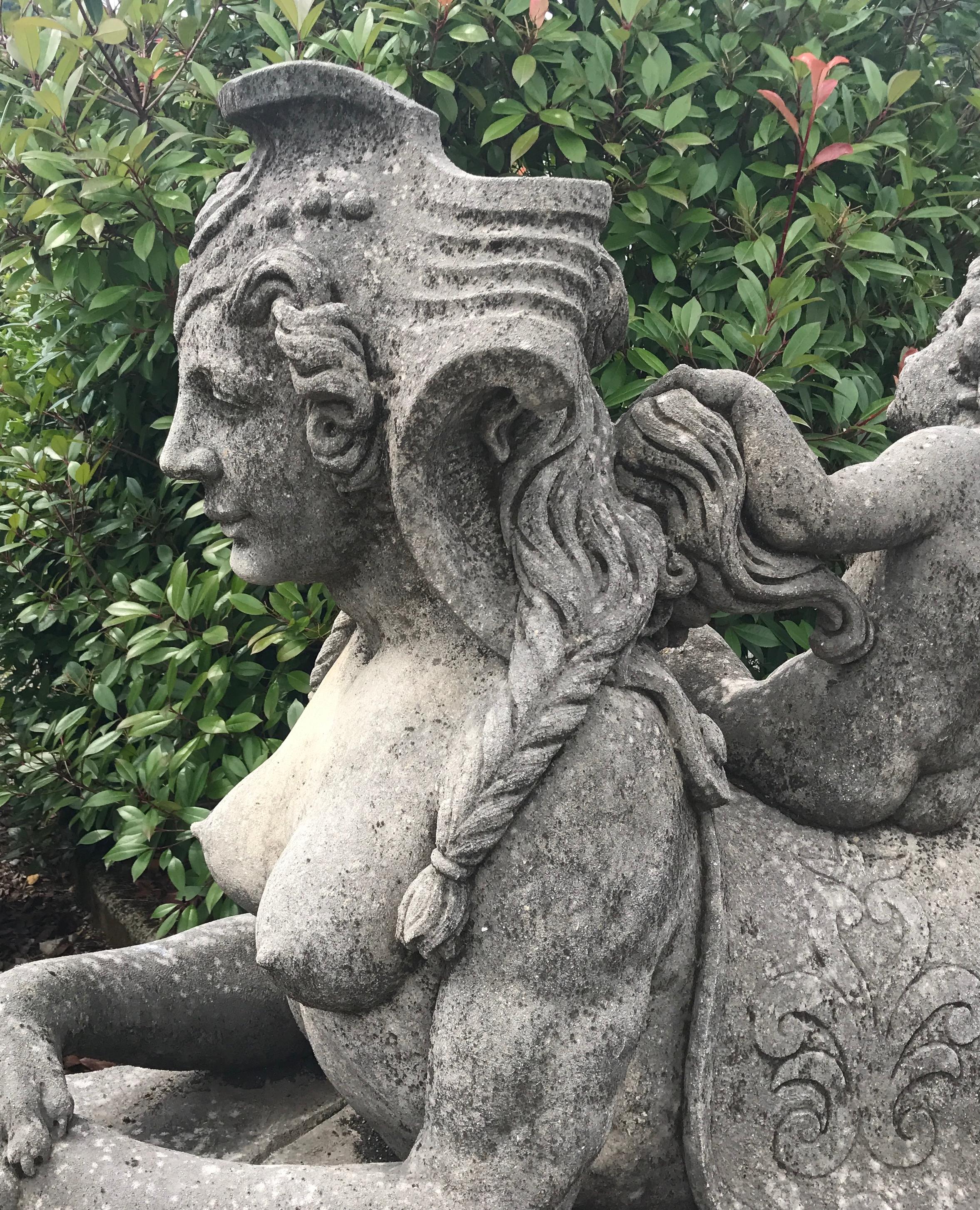Designed as entrance guardians, this pair of mythical lady sphinx statuary display the head and chest of a neoclassical woman and the body of a recumbent lion on a rectangular stone base. Very good condition with light grey patina due to age and