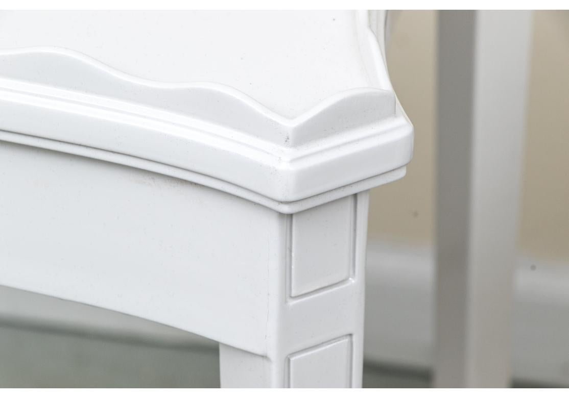 A fine pair of delicate end tables in a custom white lacquer treatment. Each is raised on squared, tapered legs with X form stretcher support. The rectangular table tops with curved ends and sides. A very decorative, scalloped gallery around the