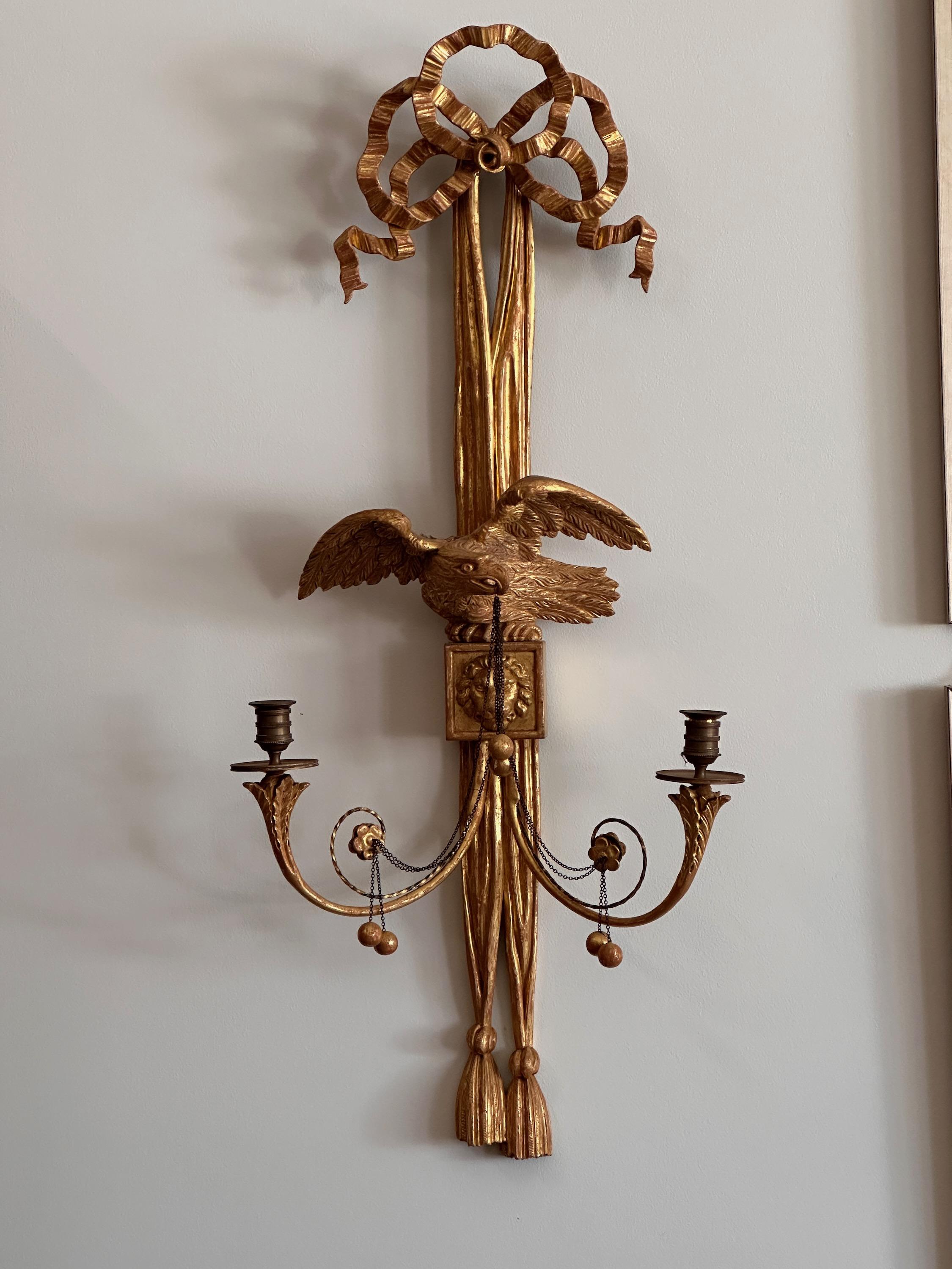 An exceptionally large pair of early 19th century English Regency carved giltwood sconces with eagles in mirror image perched on carved ribbon swags and lion's head medallions each with two candle holders.