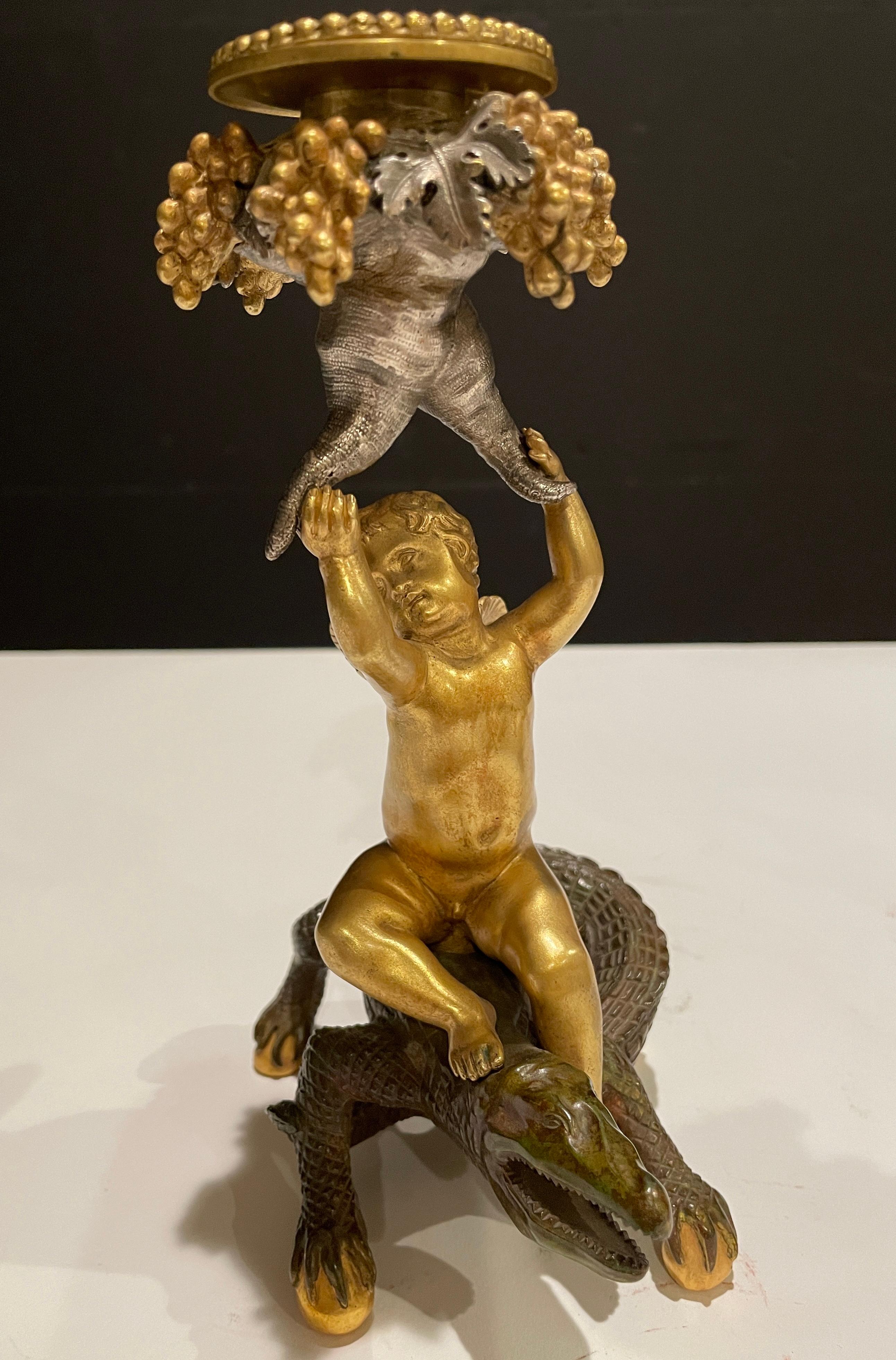 Pair of 19th century French/Austrian gilt, silvered and patinated figural exotic candlesticks. Cherub figures with angel and fairy wings seated atop a winged dragon and crocodile holding a cornucopia of grapes, vines and leaves.