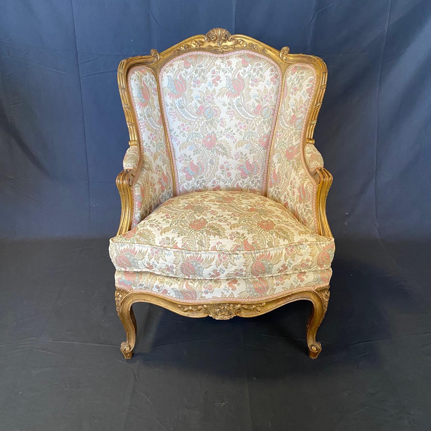 An exquisite pair of French Louis XV style giltwood bergères armchairs or wingback chairs, circa 1880,  having carved floral motifs, cabriole legs and vintage upholstery in very good condition.  Each chair is adorned with intricately carved floral