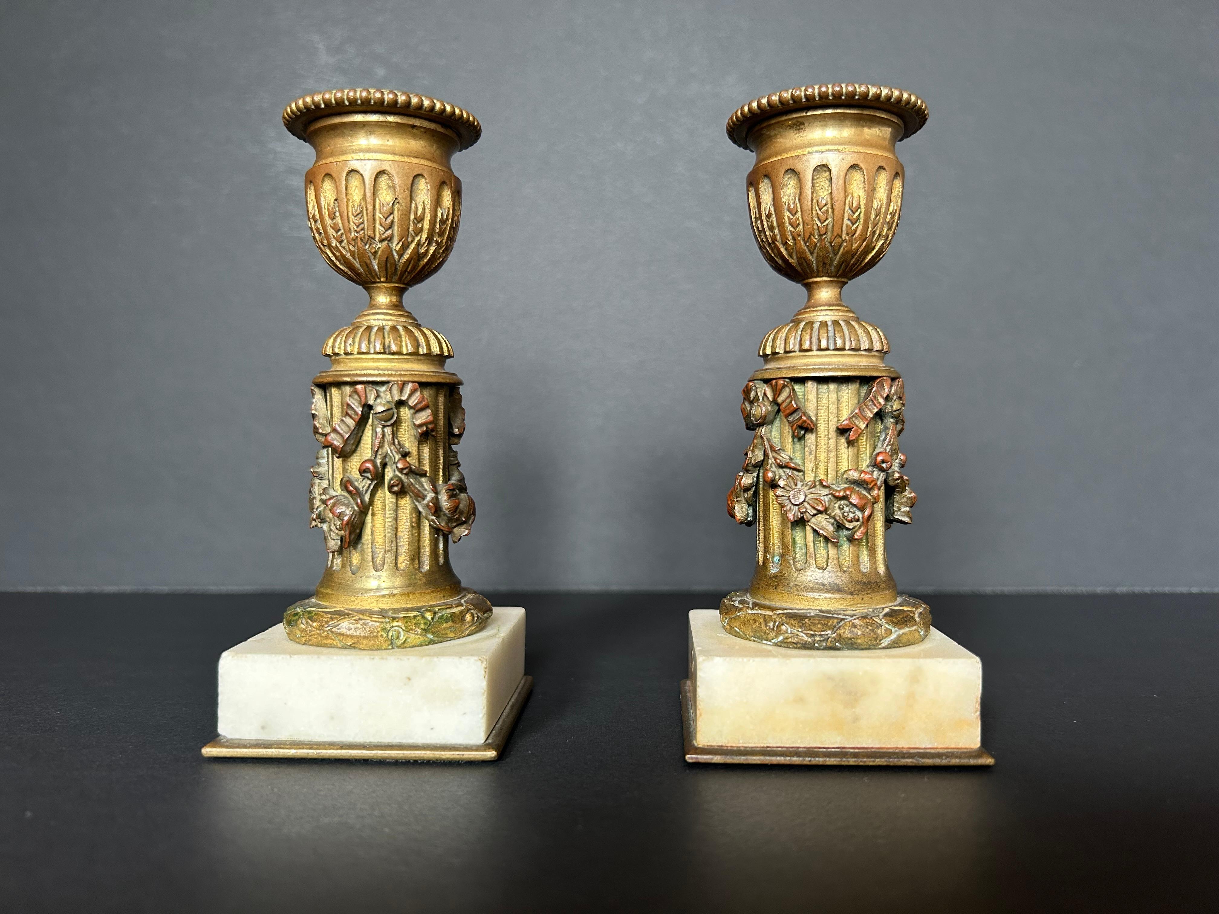 An exquisite pair of early nineteenth century small candlesticks from France, made of gilt bronze on small, square alabaster bases. These candlesticks feature neoclassical columns swagged in flower garlands and ribbons, surmounted by two intricately