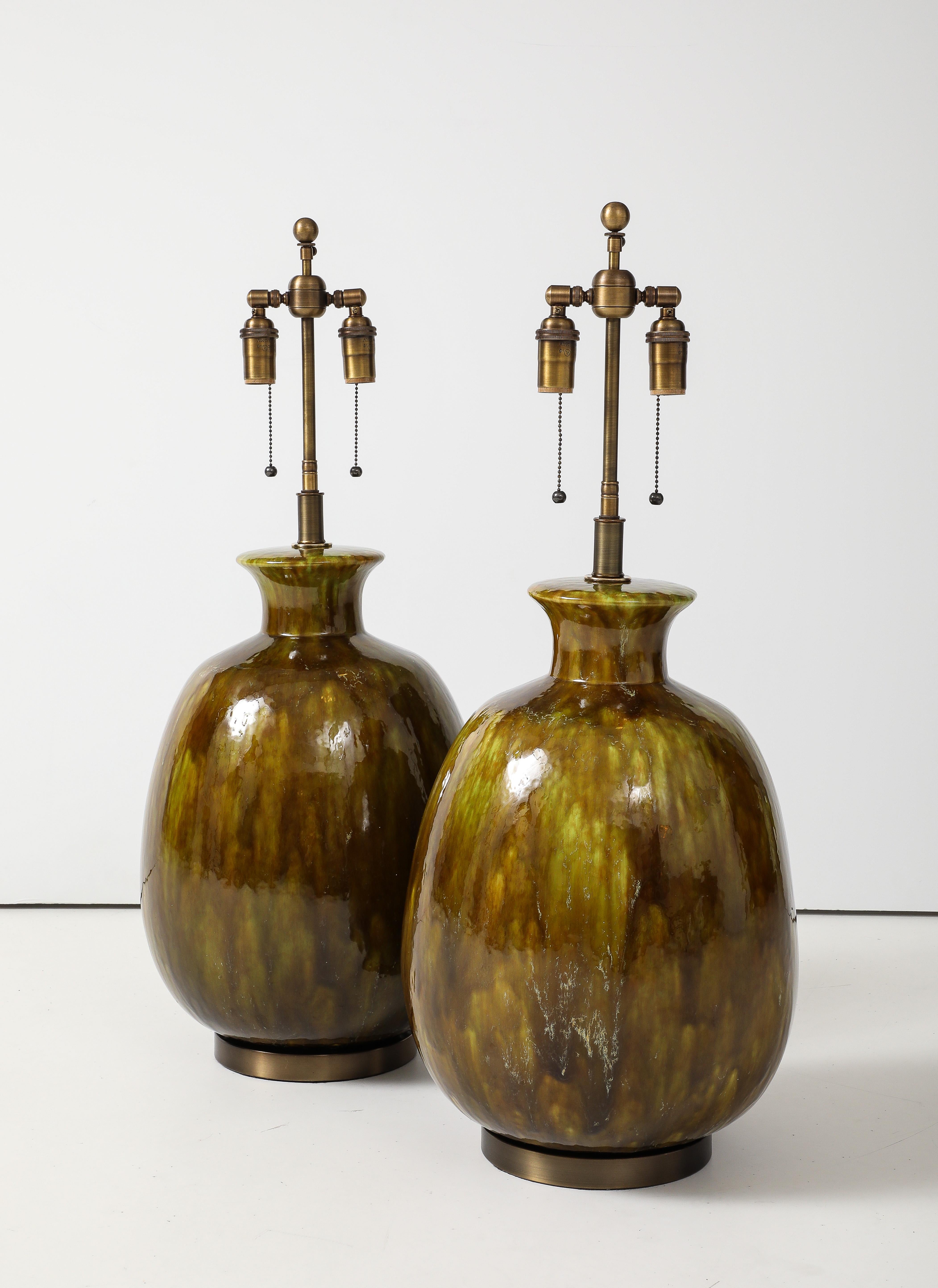 Très grande paire de lampes en céramique avec une magnifique glaçure de couleur mousse.
Les corps de lampe bulbeux en céramique reposent sur des bases en laiton antique. 
recâblée avec des doubles grappes réglables en laiton antique qui acceptent