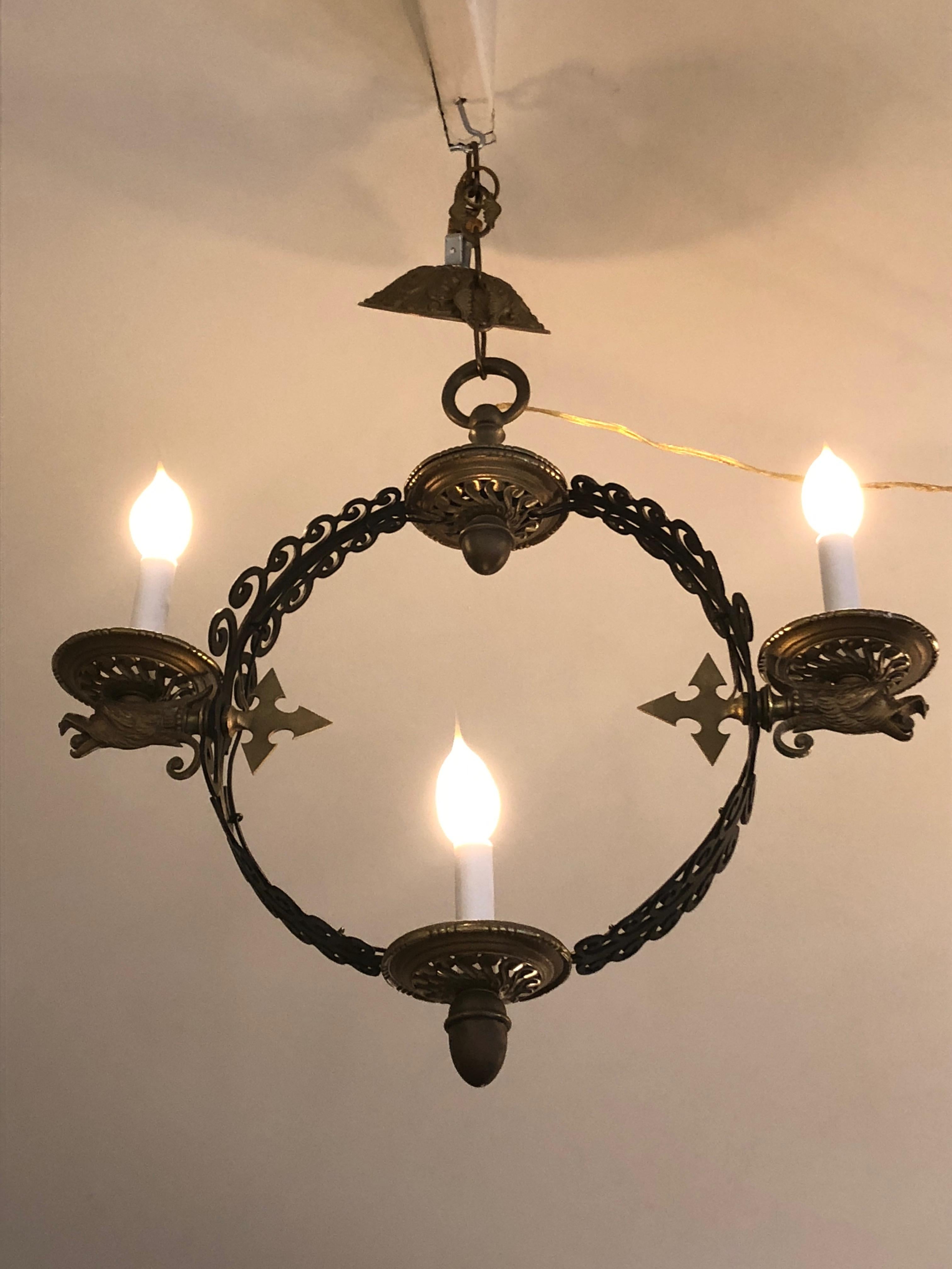 A pair of rare iron and antiqued brass light fixtures having an open circle with iron curlicue scrollwork, around which three candlestick lights are set on brass candle cups. Accenting the candles are amazing spearhead and falcon head motifs. Fully