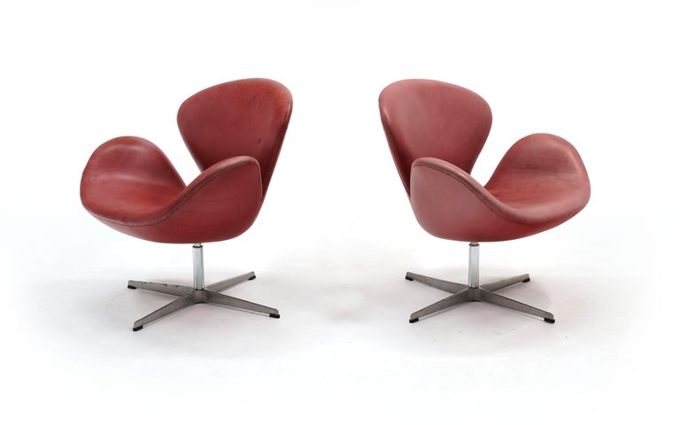 Pair of Arne Jacobsen Swivel Swan chairs in the original red leather. The leather is faded to a unique soft light red color. Please see photos. The first photo looks more red than they really are but as you look at the additional photos you will see