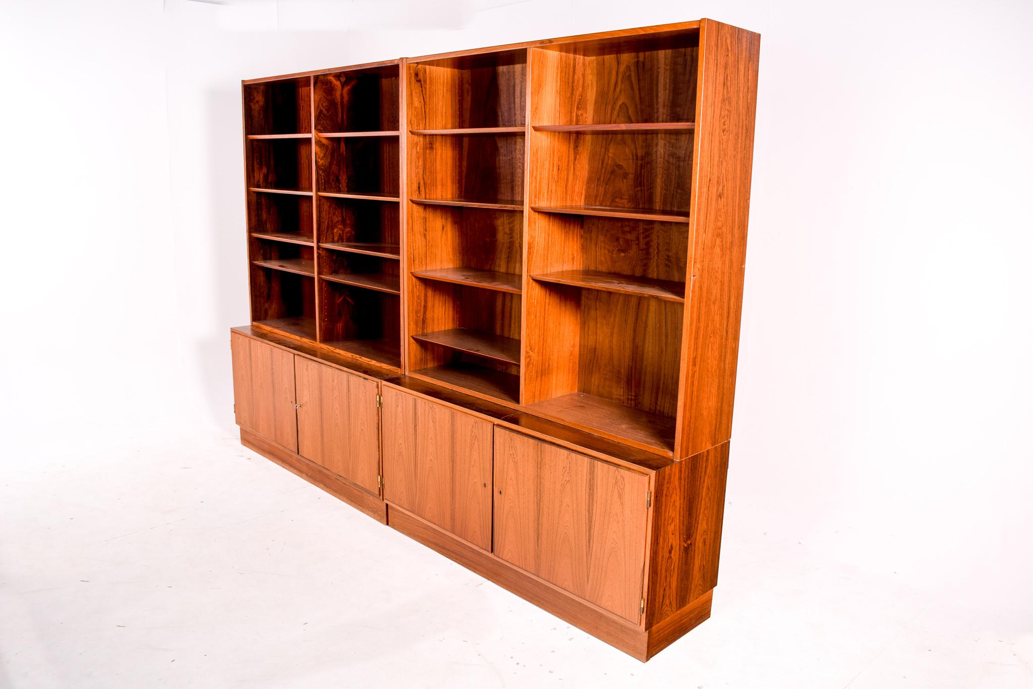 This Danish modern bookshelves unit features original rosewood veneer finish with upper open shelving and closed cabinet space below. A pair of rosewood two-part storage cabinet and bookcase; locking lower cabinet with divided bookcase, each with