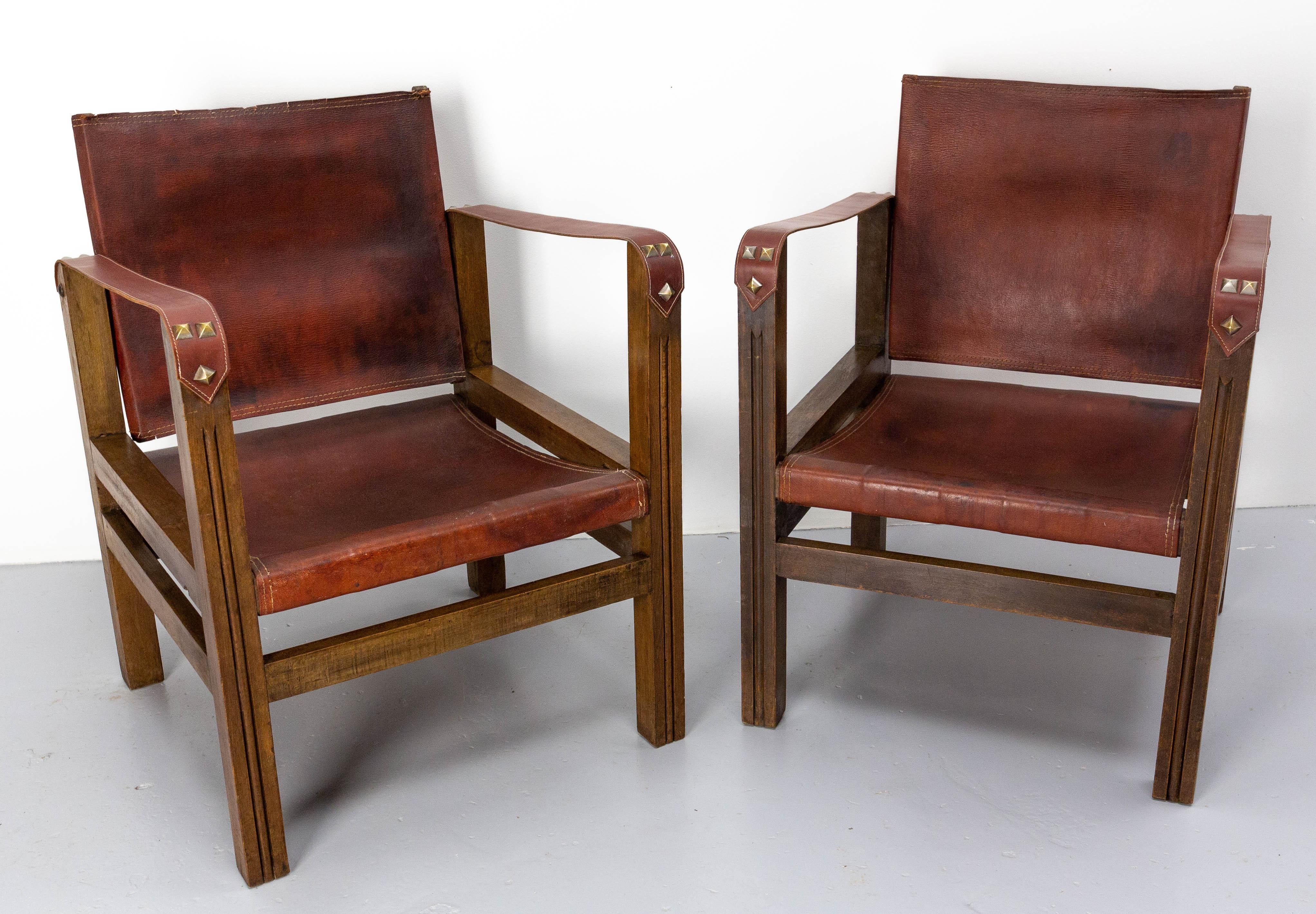 Paire de fauteuils ouverts ou chaises de bureau de style safari.
Les accoudoirs ont été remplacés par un cuir rouge similaire et patinés.
Un petit manque sur l'un des dossiers, et des marques d'usage qui donnent la patine aux chaises. (voir