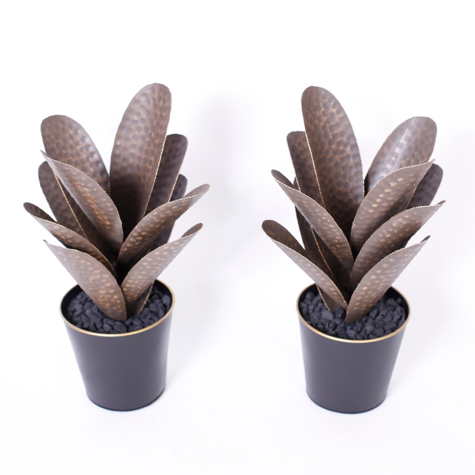 Pair of faux agave plants crafted in brass with a contrived patina and serrated edges set in metal planters with faux black rocks.