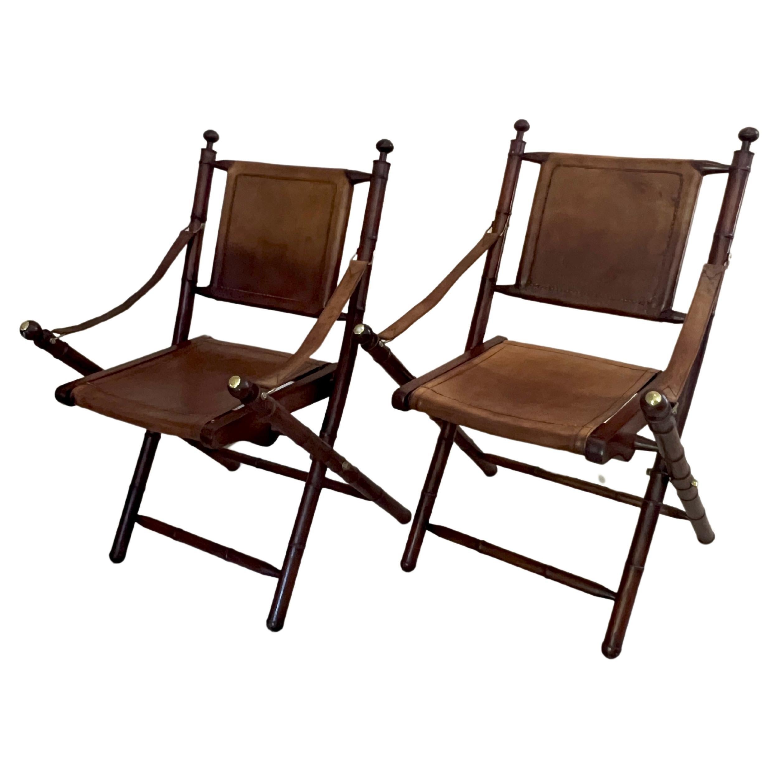 Pair of faux bamboo leather and wood folding campaign chairs with brass hardware on the arm straps and brass details in the back and arm, finials.

The pair are quite handsome and work in many spaces.  Due to the versatility of folding they can be