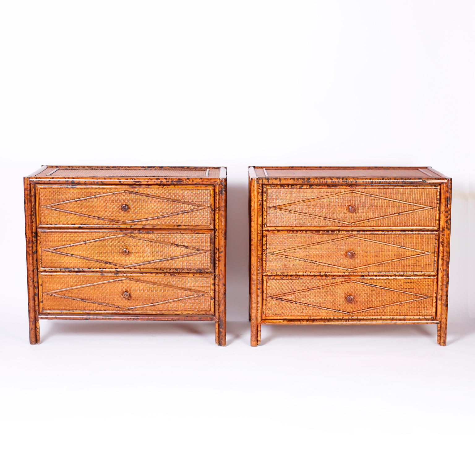 Pair of three drawer British Colonial style stands with faux burnt bamboo frames and grasscloth panels on the tops, sides, and drawer fronts under applied geometric designs.