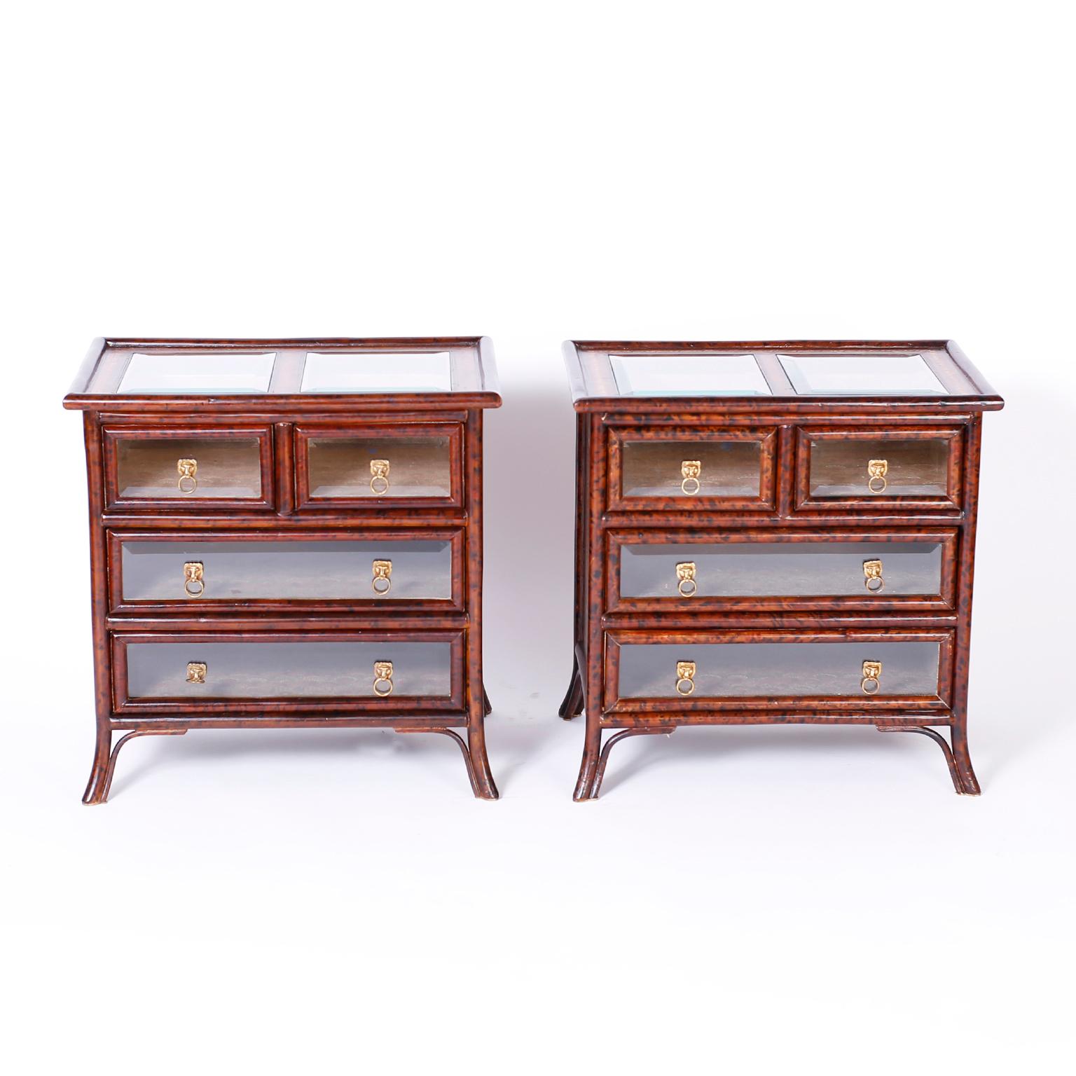 British colonial style stands with faux tortoise bamboo frames and tooled leather panels on the sides and back, featuring bevelled glass panes on the top and four drawer fronts. The drawers are lined with marbleized book paper and have brass lion's