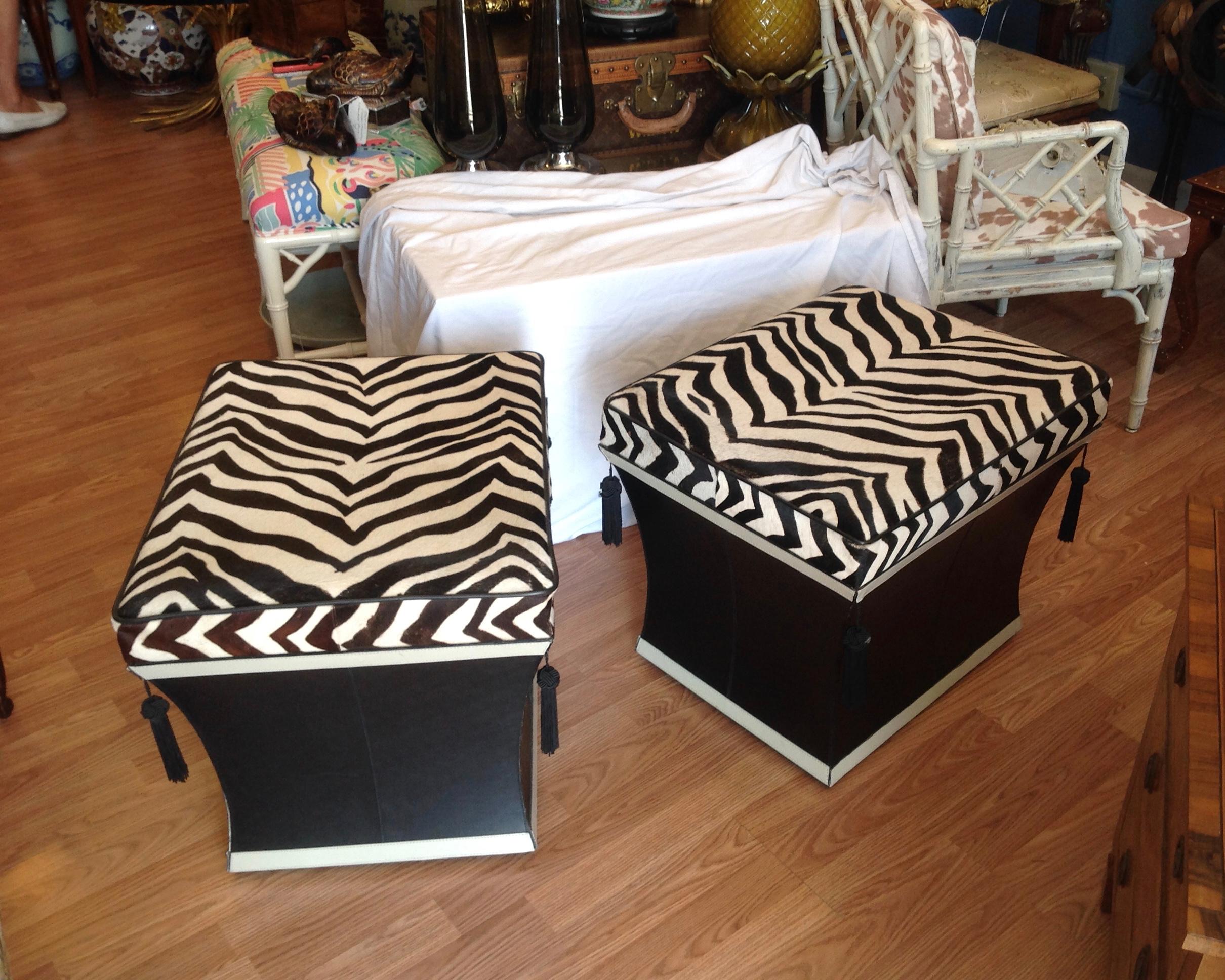 An eye catching pair of hide and leather ottomans, appointed with tassels,
and fashioned with hinged tops to provide storage inside - great form and function.