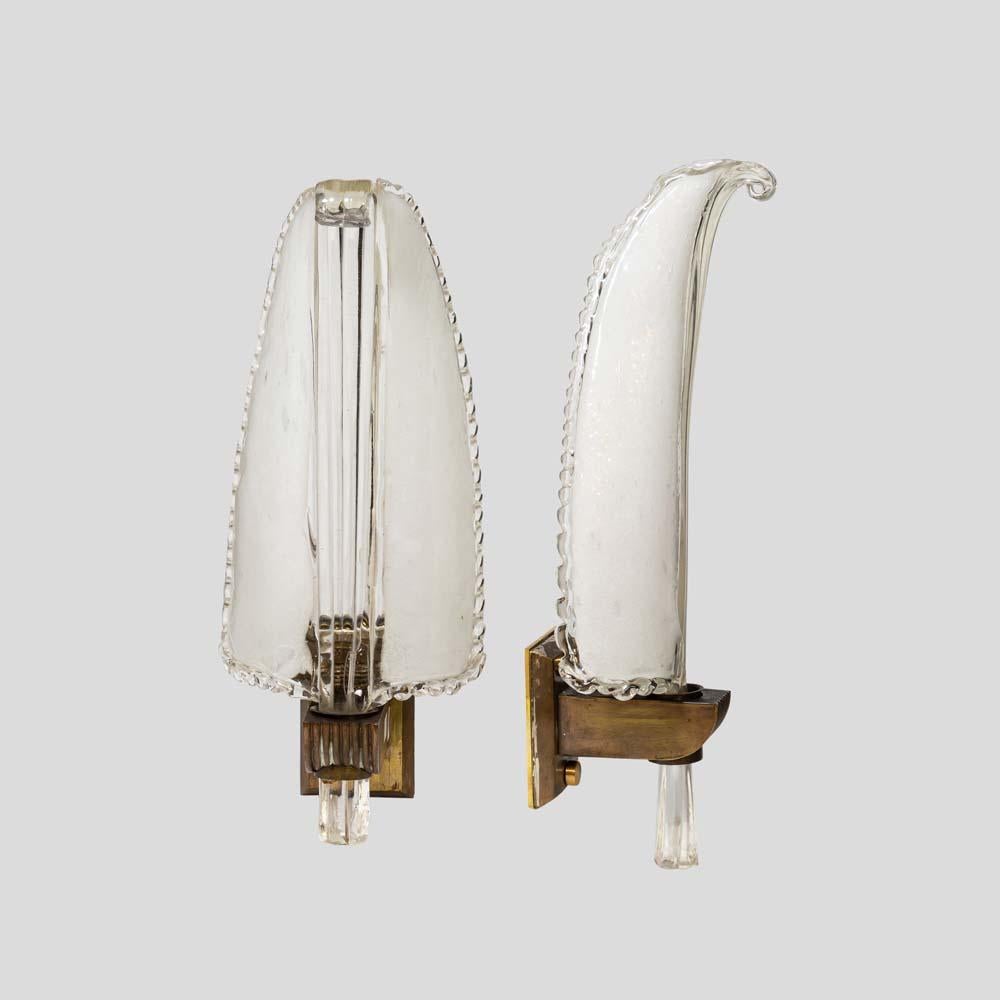 These stunning wall lights feature a pair of feather-shaped glass shades, hand blown from clear and frosted white glass. The shades elegantly mount on an original brass structure, creating a beautiful contrast. One of the glass shades has a longer
