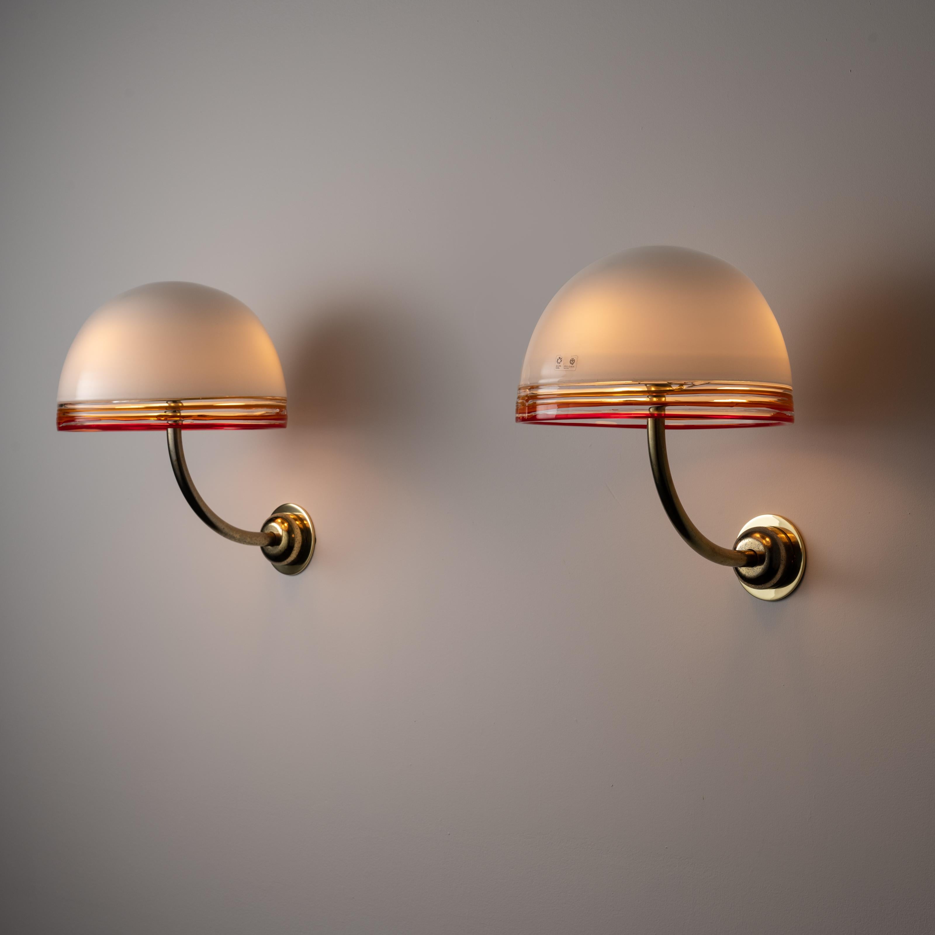 Pair of wall lamps by Roberto Pamio for Leucos. Designed and manufactured in Italy, circa 1970. Robust pair of wall sconces with upward sloping brass necks and frosted glass shades with orange and red ribbed accents on the lip of each shade. The