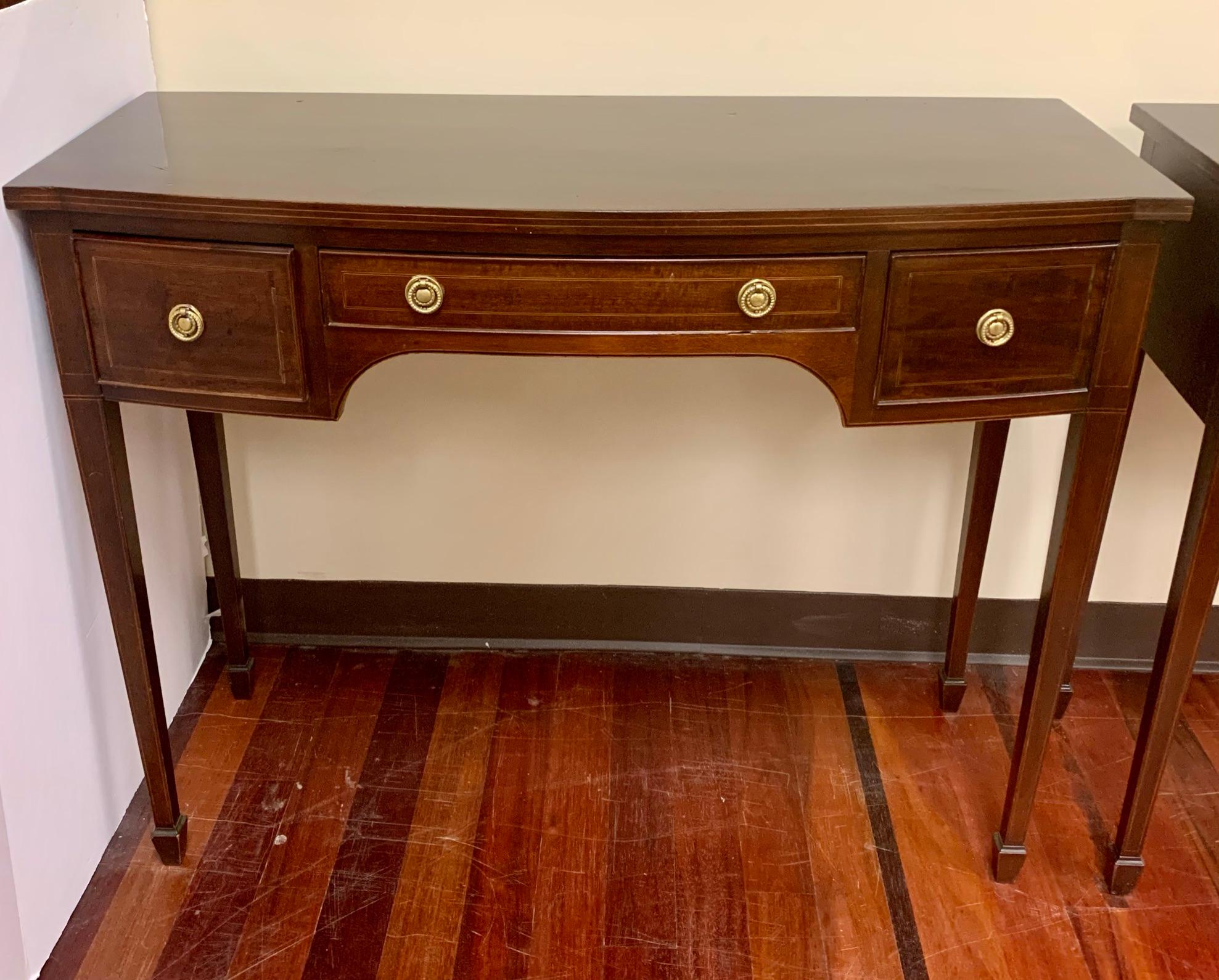 Matching pair of Classic Federal style mahogany console tables with curved front and three drawers. They feature fine line inlay on the front, drawers and legs and original brass pulls on the dovetailed drawers.