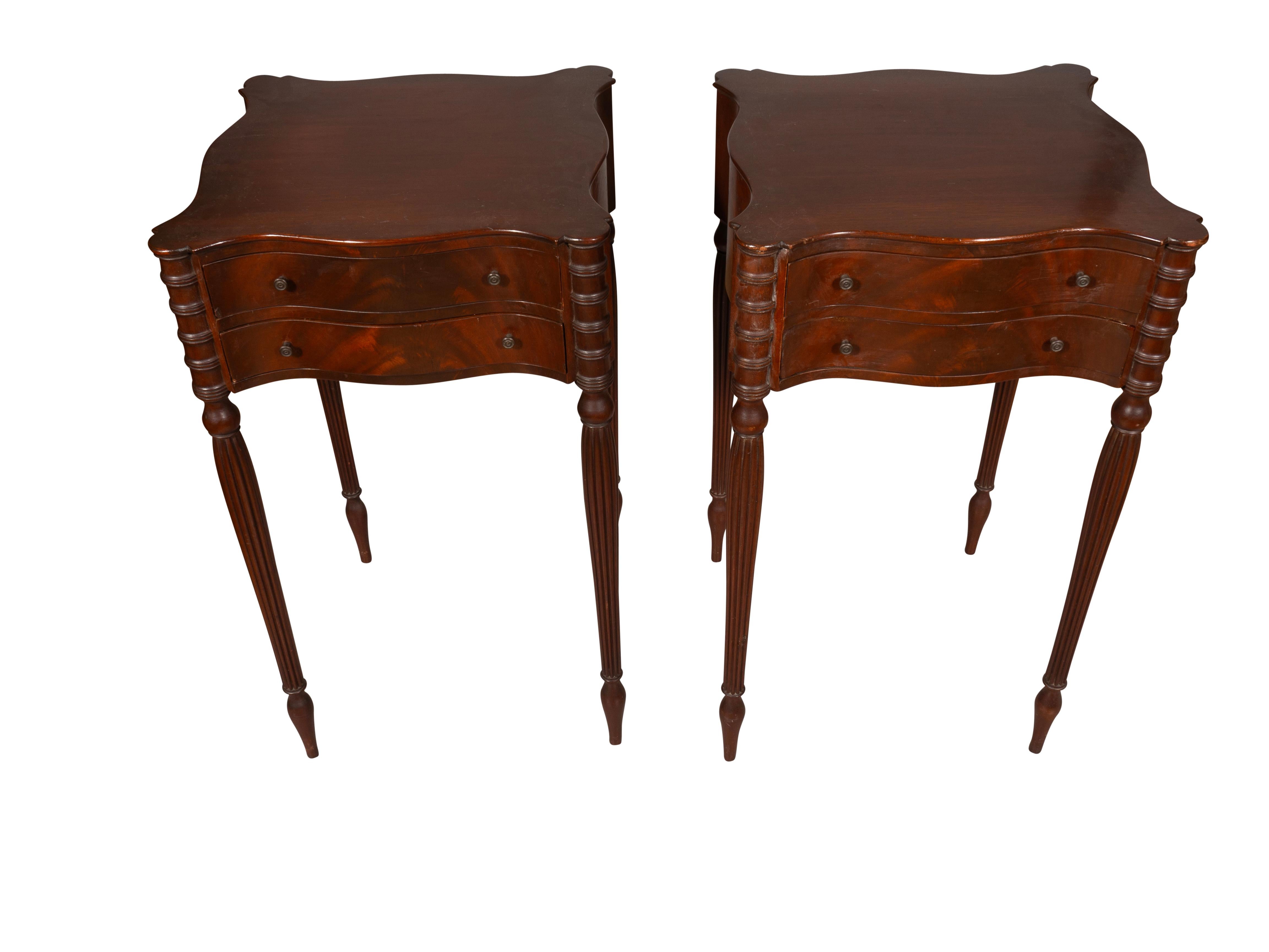 Each with shaped square tops and rounded corners. Two conforming drawers and raised on reeded tapered legs.