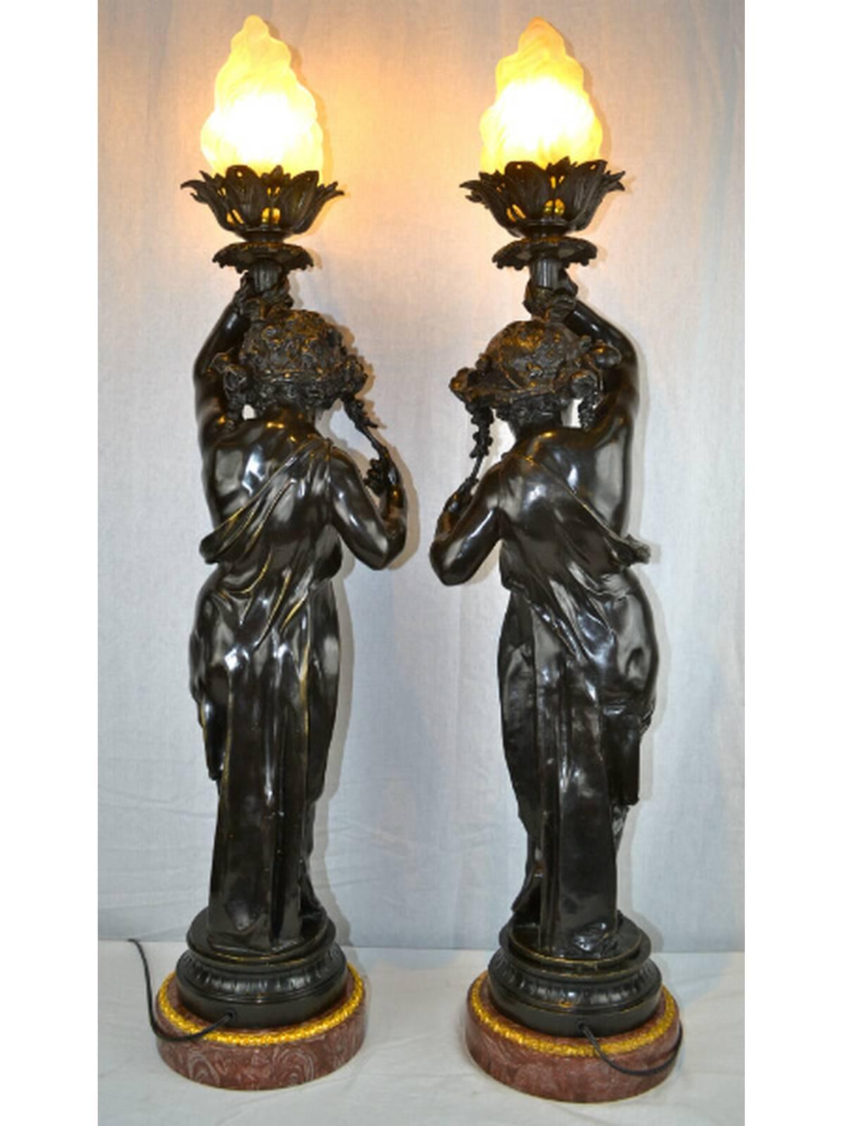 A beautifully cast matching pair of patinated bronze figural torcheres in the manner of Claude Michel Clodion, modelled as classically draped young girls with garlands of flowers in their hair and holding a flame torch. Set on a round marble base