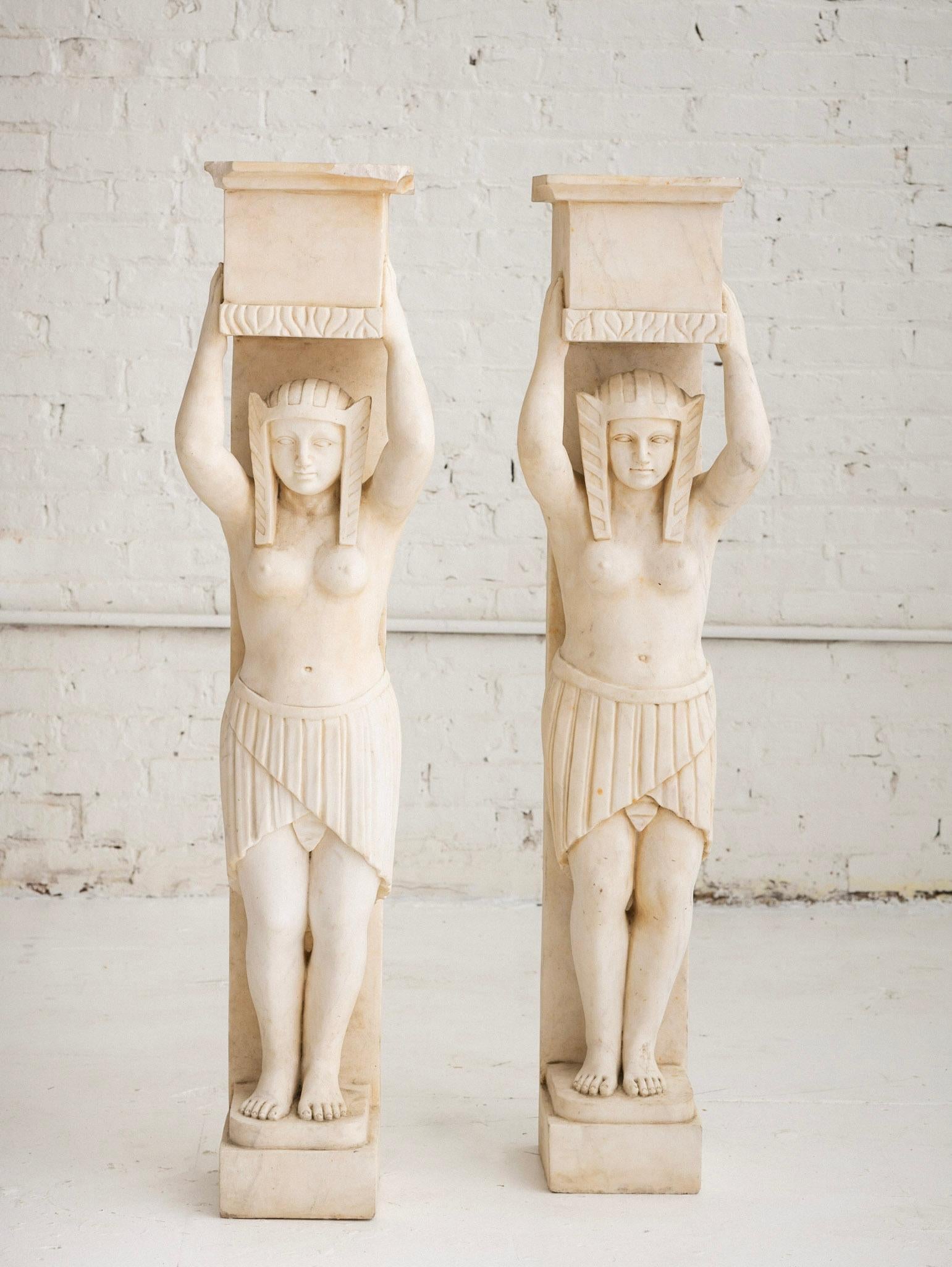 Pair of antique fireplace surrounds carved of solid white marble into two female Egyptian style figures. Unfinished backs and top surface. As architectural salvage, these may be repurposed as pedestals, plant stands or simply objet d’art. Dimensions