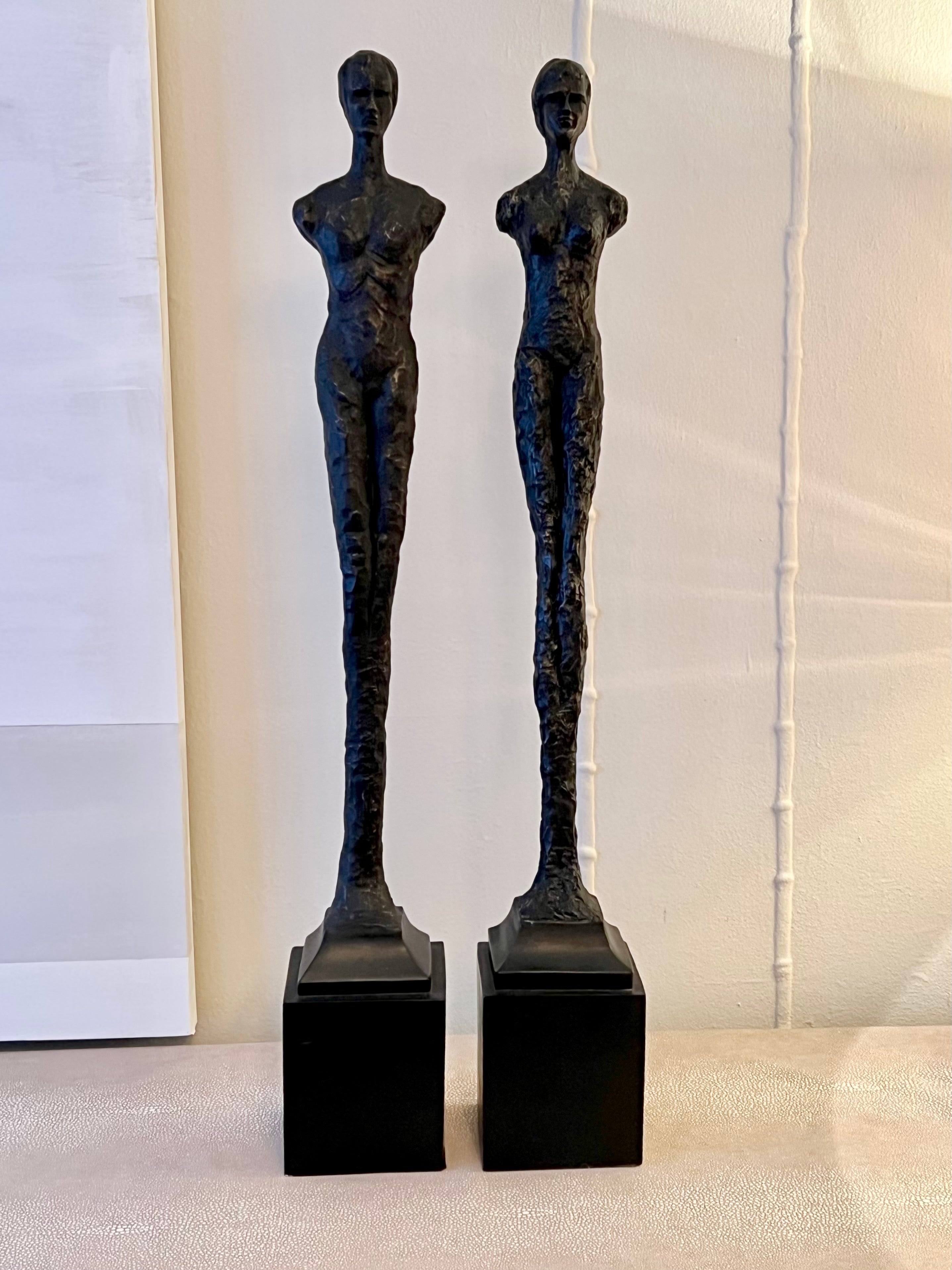 Two slender nude Resin figurative statues on wooden bases. In the style of Giacometti - these delicate figure have a pinched-clay look. They stand nearly 3' tall, impressive and thoughtful in many rooms. A compliment to many interiors and settings -