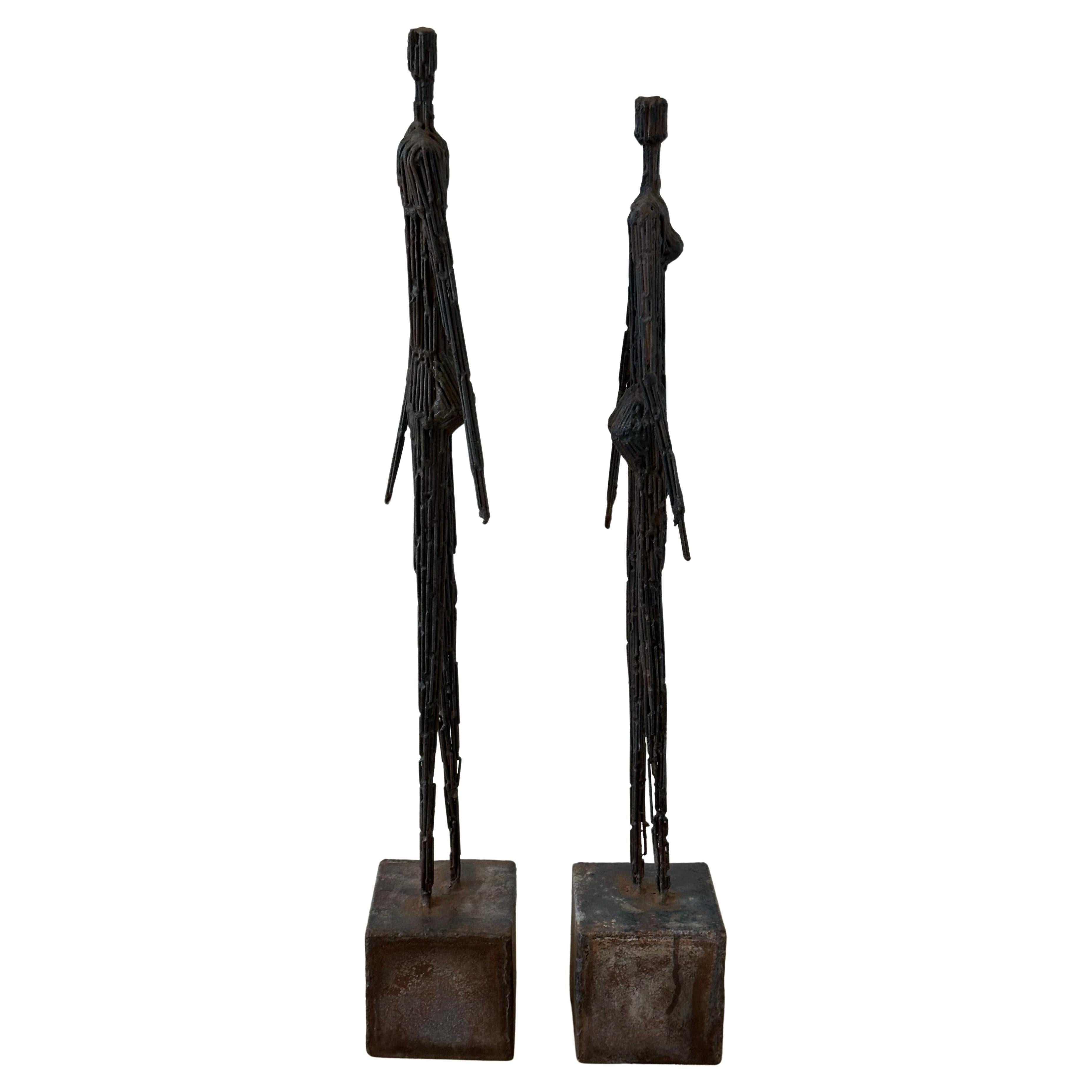 Coppia di sculture figurative brutaliste in metallo saldato, uomo e donna, nello stile di Giacometti, circa anni Settanta. Le sculture poggiano su basi in metallo consumato di 4 