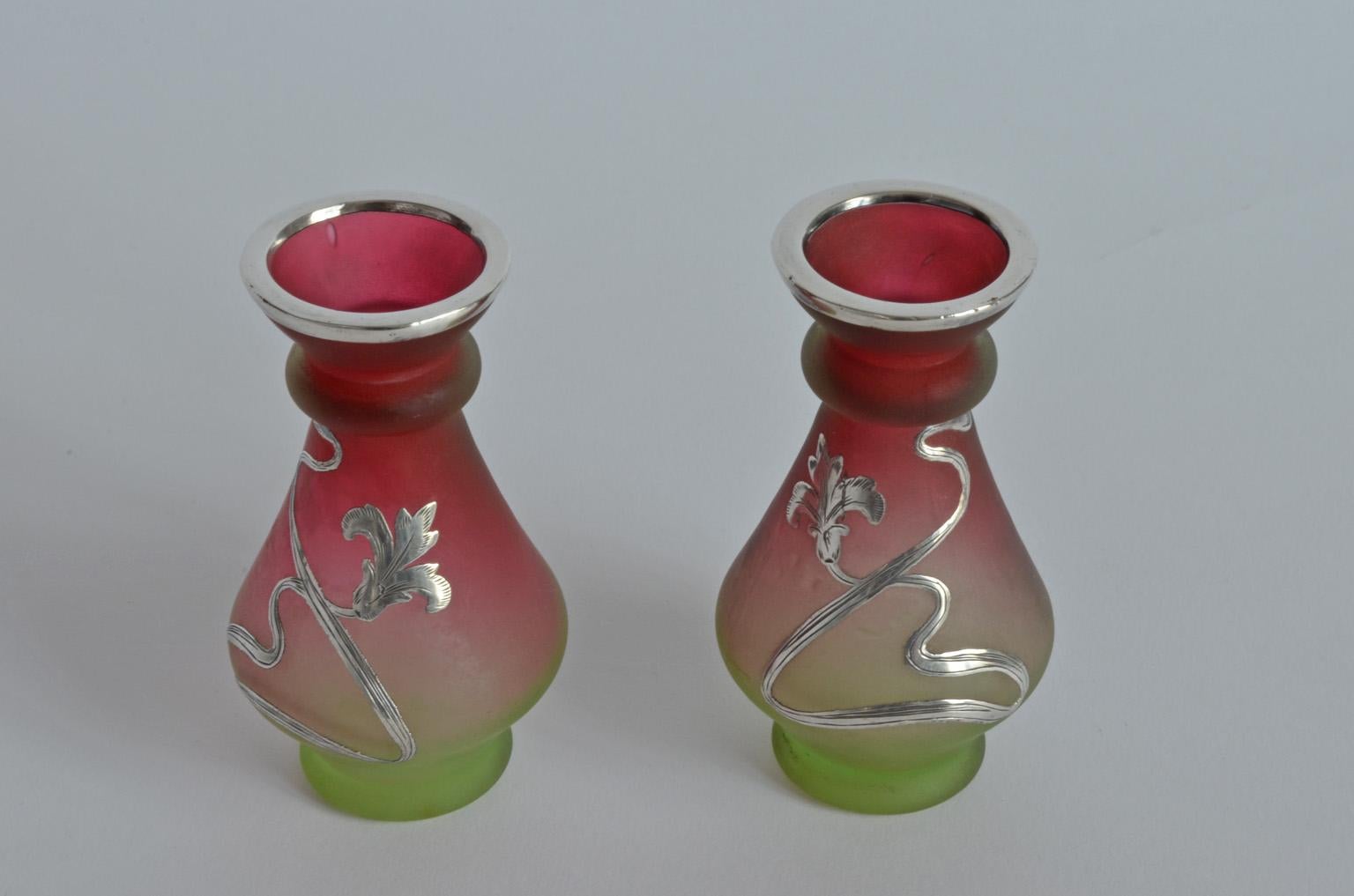 Pair of Fine Art Nouveau silver overlay miniature glass vases Bohemia, 1900s.
Silver rim with etched silver, Art Nouveau.
Green and ruby / burgundy red glass.
Vine and leaf design on the sides, unmarked.
 