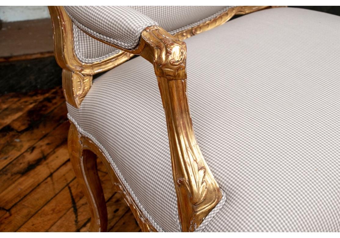 Classic French fauteuils, fine craftsmanship with 18th century style carved, gessoed and gilt frames with leafy crests, the scrolled arms with leaves. The legs with carved palmette knees and the shaped skirts with carved leafy cartouches. Custom