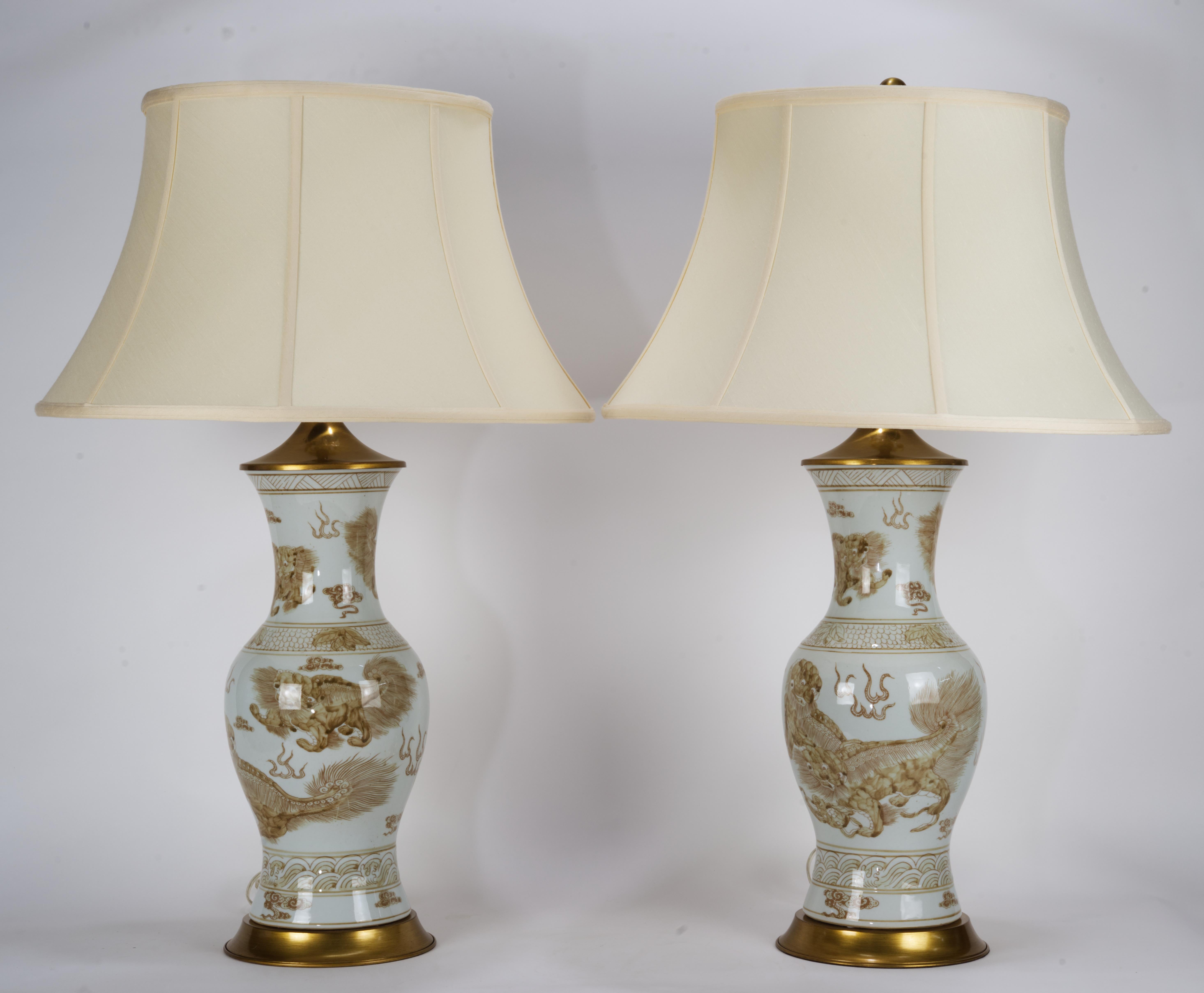  Large chinoiserie style white and brass brown table lamps are mounted on round brass bases and topped with fine brass fittings and substantial round brass finials. Classic urn vase shaped bodies are decorated with traditional Chinese motifs and
