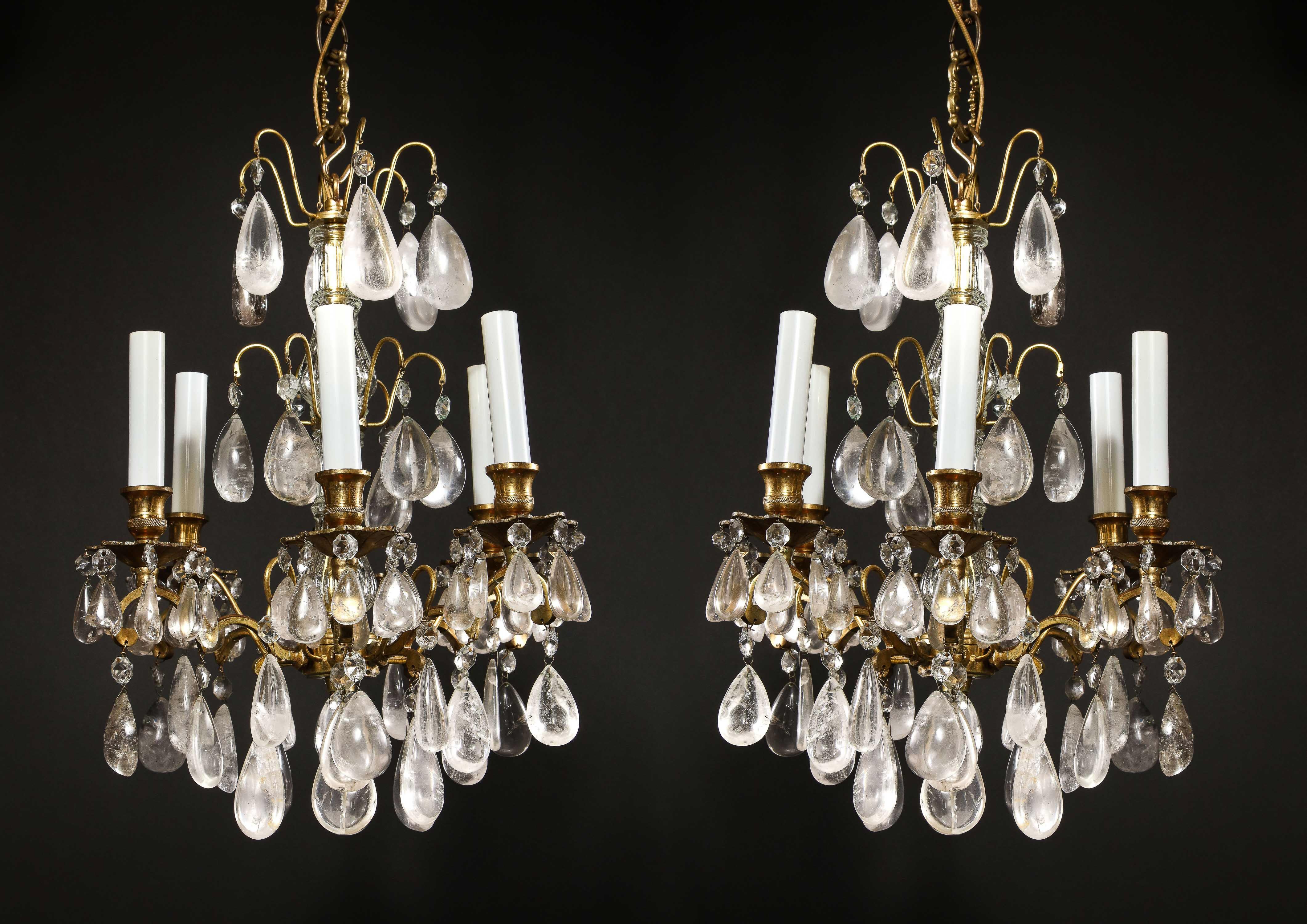 A pair of continental Louis XVI style bronze and rock crystal multi light triple tier chandeliers embellished with cut rock crystal prisms.