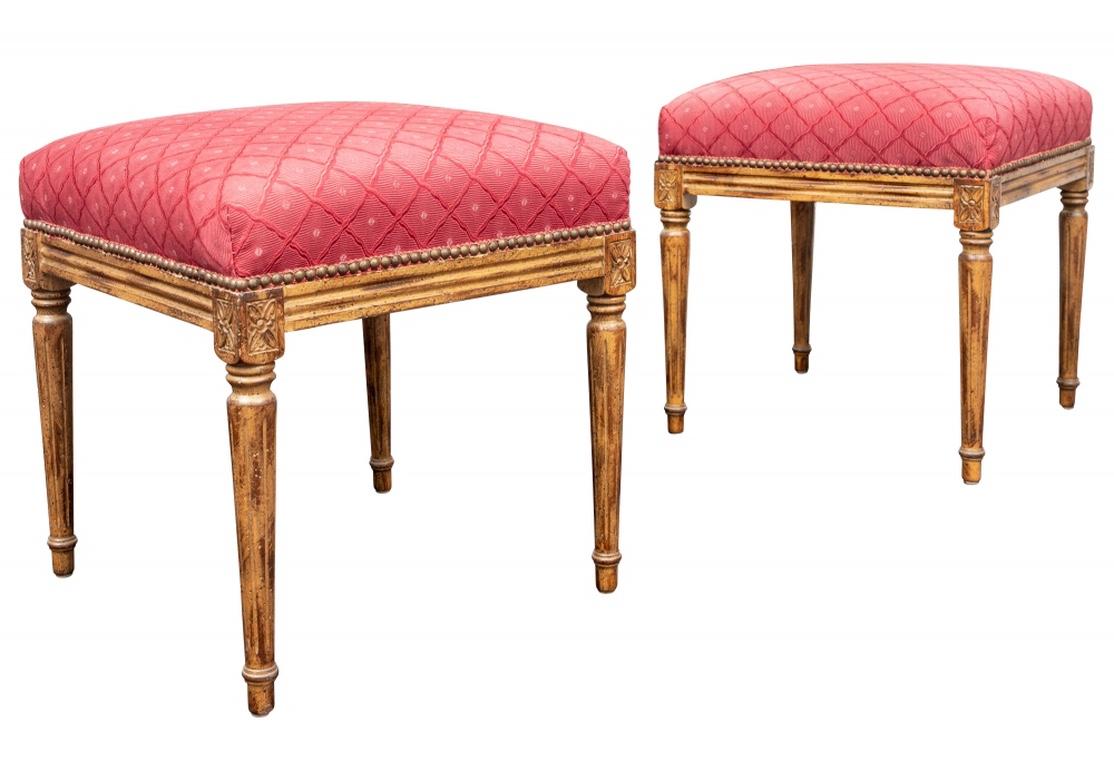 A fine pair of French Style Footstools. In a Walnut finish, the carved frames in the Louis XVI style with cylindrical fluted tapering legs and rosettes at the tops. The seats upholstered in a fine soft red lattice pattern fabric with nail head trim.