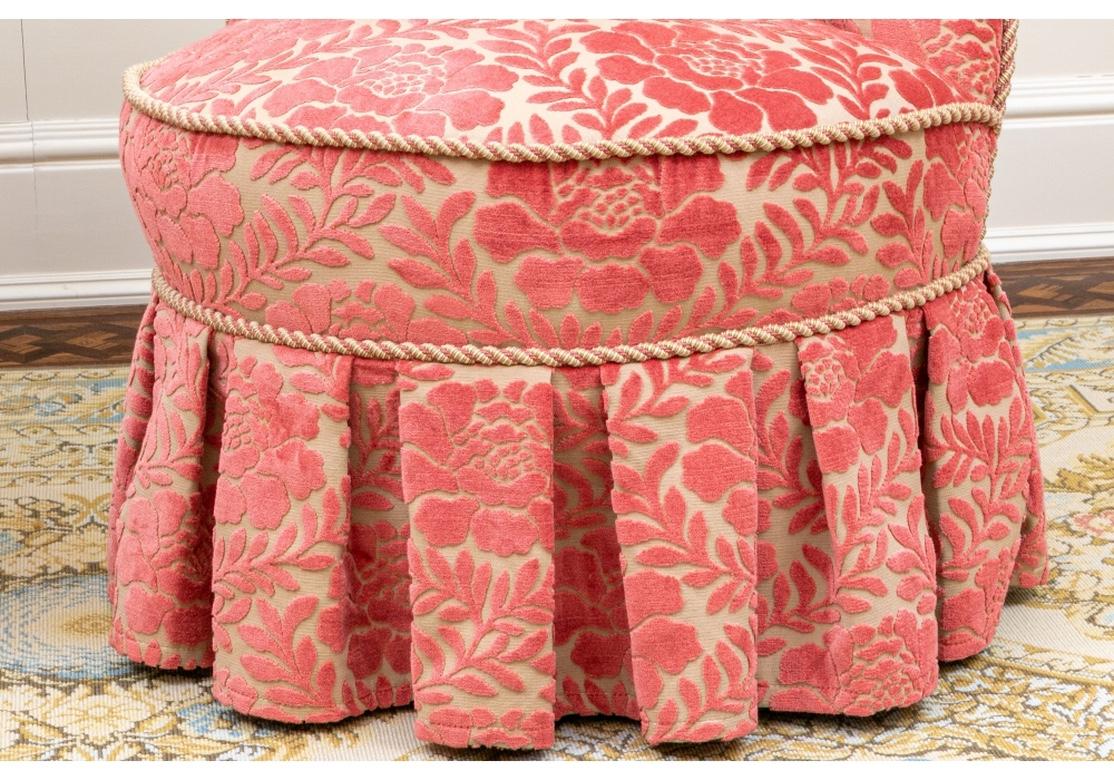 An impeccably upholstered pair in striking color. Elegant and comfortable oval tufted back Fireside Chairs raised on tapering square wood legs. Upholstered in a coral on pale tan cut velvet type fabric in a floral pattern. With deep pleated skirts