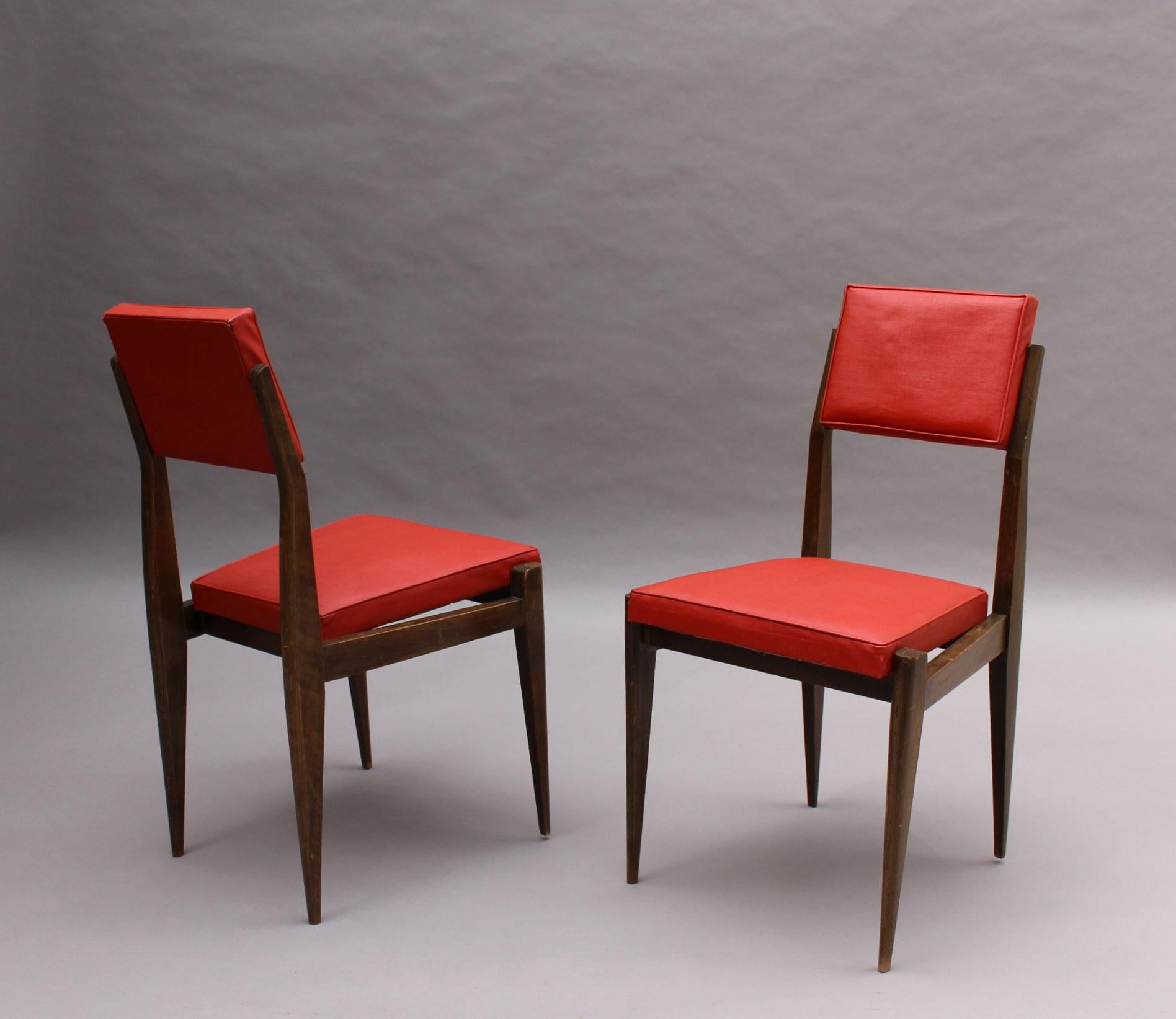A pair of French mid-century stained beech chairs with original red vinyl upholstery.
