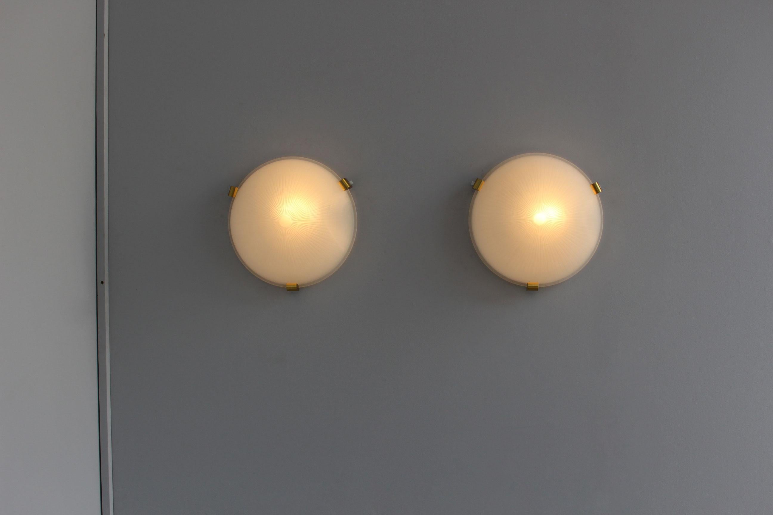 A pair of fine French Art Deco flush mount ceiling fixtures or wall sconces by Jean Perzel, with a round optical fluted frosted glass shade supported by three bronze studs.
          
