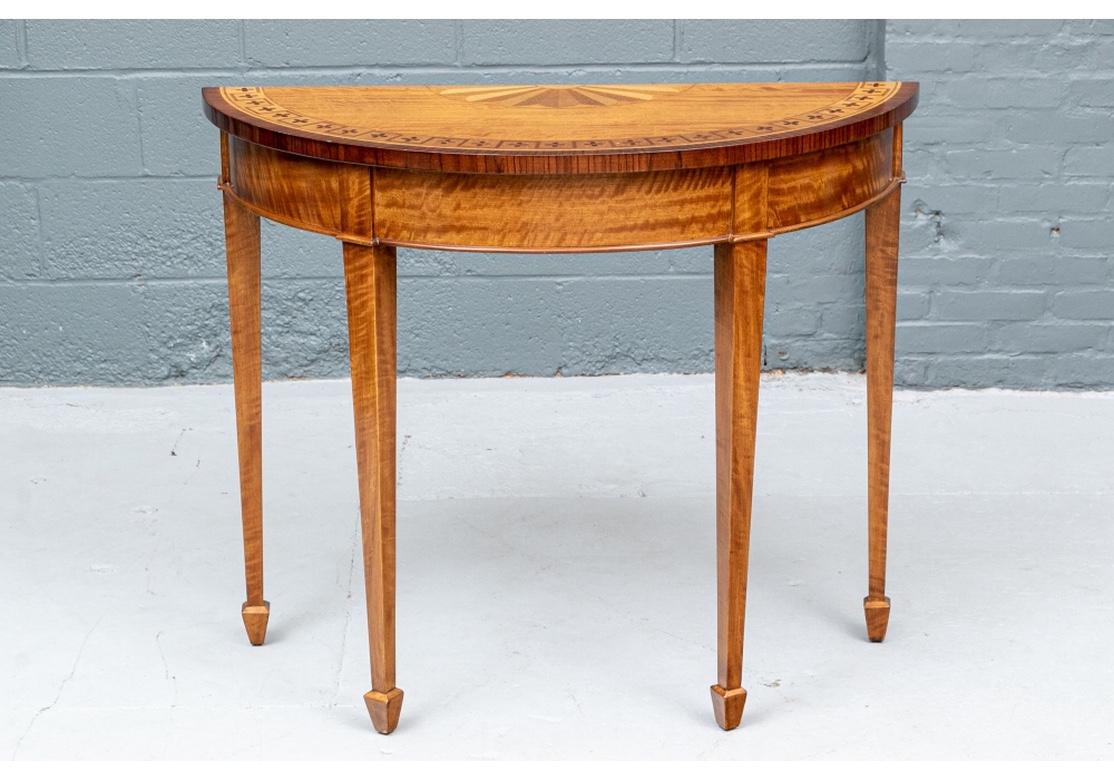 Fine pair of demilune consoles with two- tone half fan inlays at the backs of the tops. The fronts banded with inner dark cross motifs and darker mahogany outer bands and edges. Plain birch aprons and raised on square tapering legs with spade feet.
