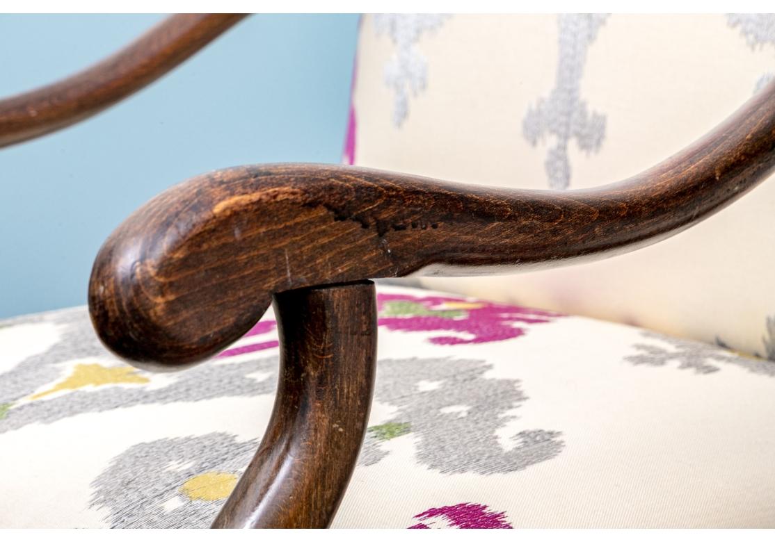 Pair of Louis XIV style walnut fauteuils with sinuous arms, arched tight back and seat. The chairs upholstered in an embroidered fabric with purple stylized flowers and floral abstractions. The chairs with scrolling cross stretcher and rose colored
